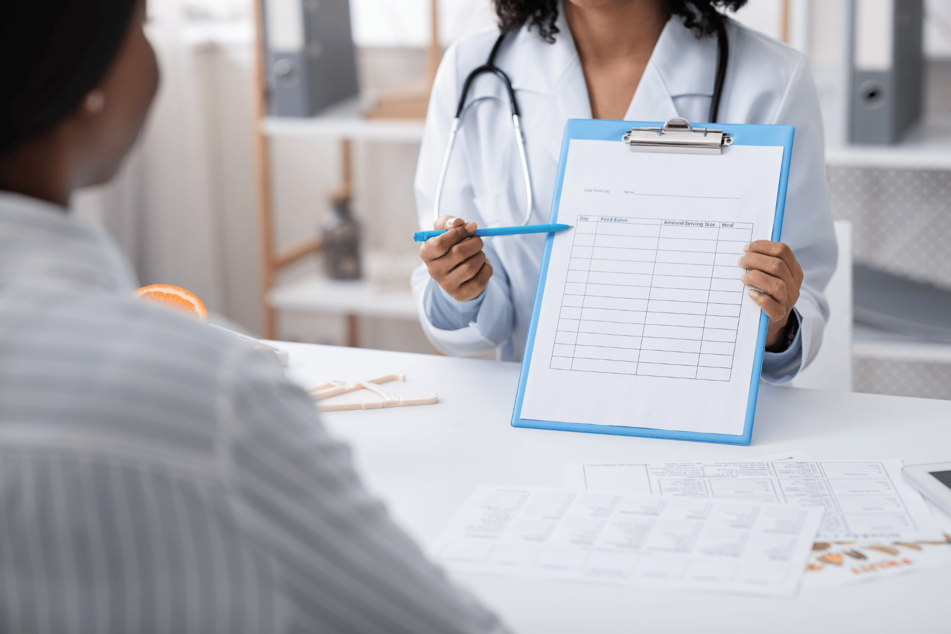 Doctor showing a patient a diet or food log form on a clipboard during consultation.