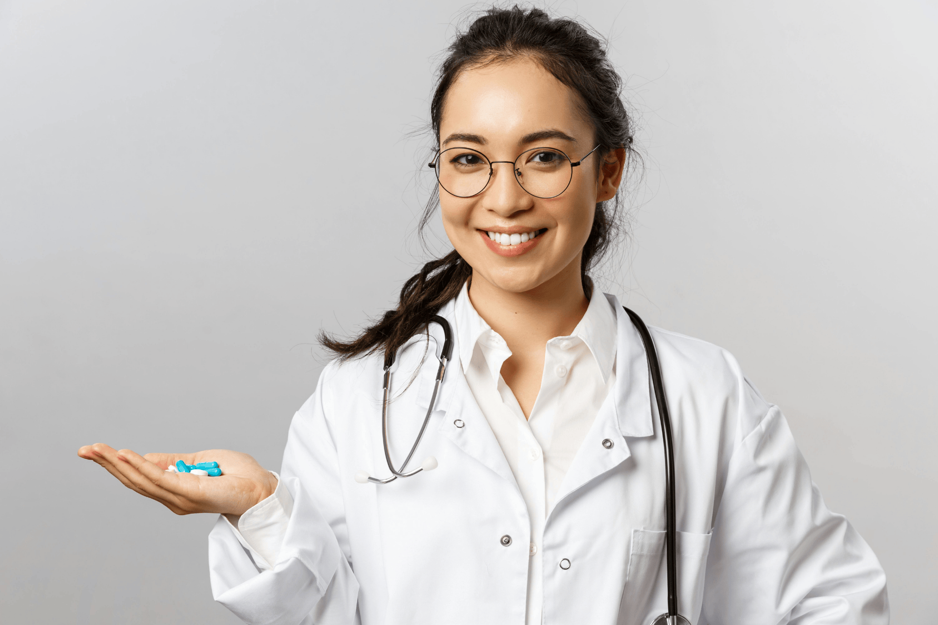 Smiling doctor holding blue and white capsules in her hand.