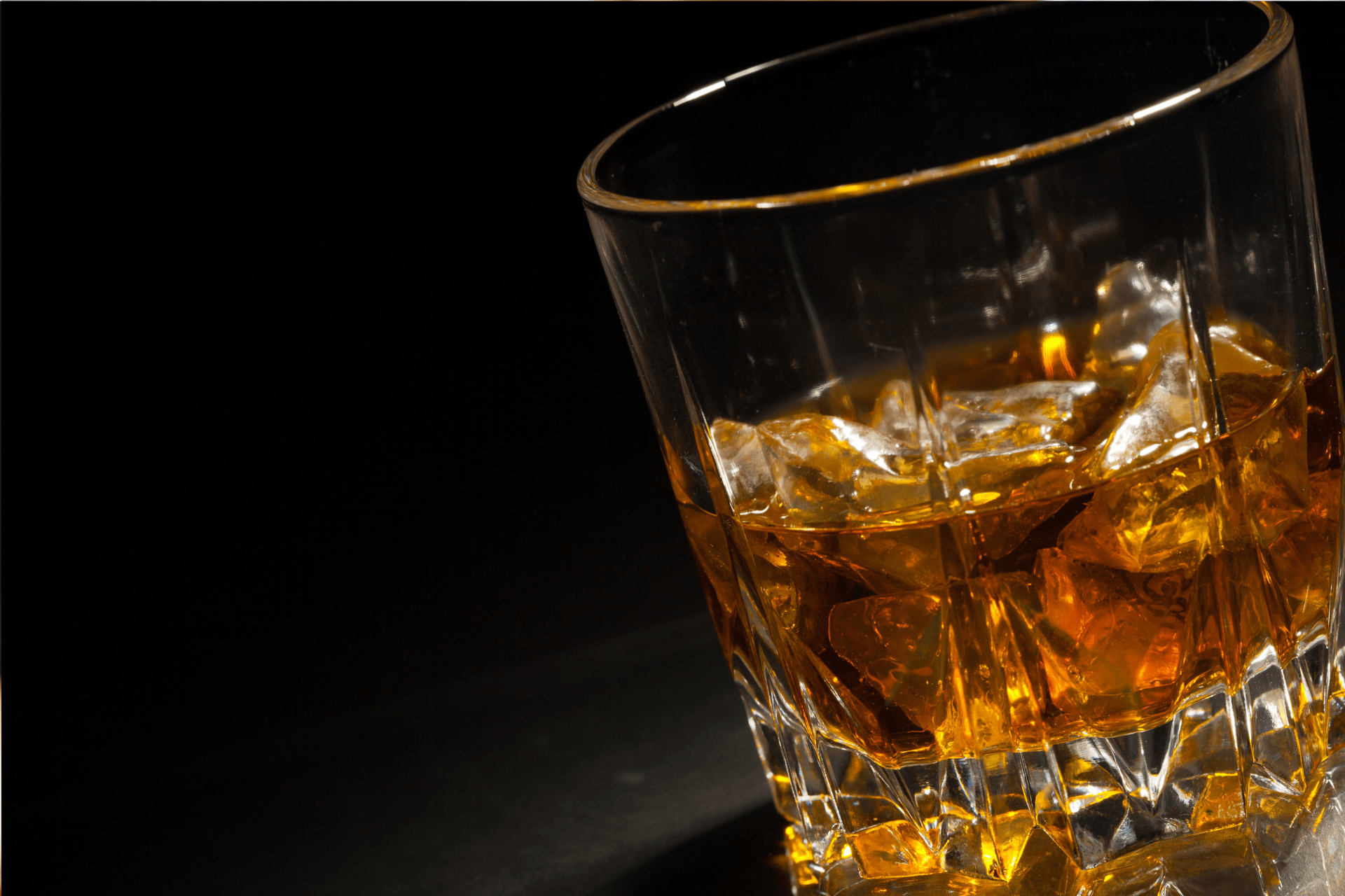 Glass of whiskey with ice cubes against a dark background.