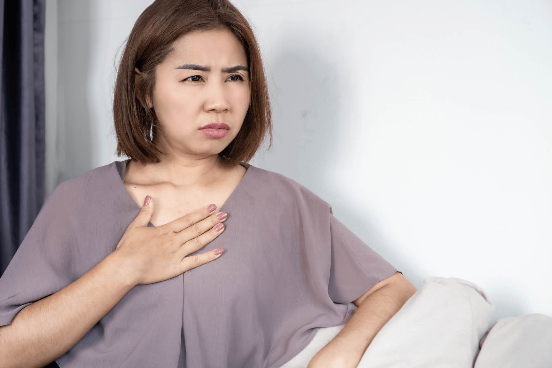 Woman touching her chest and appearing to experience discomfort or heartburn.