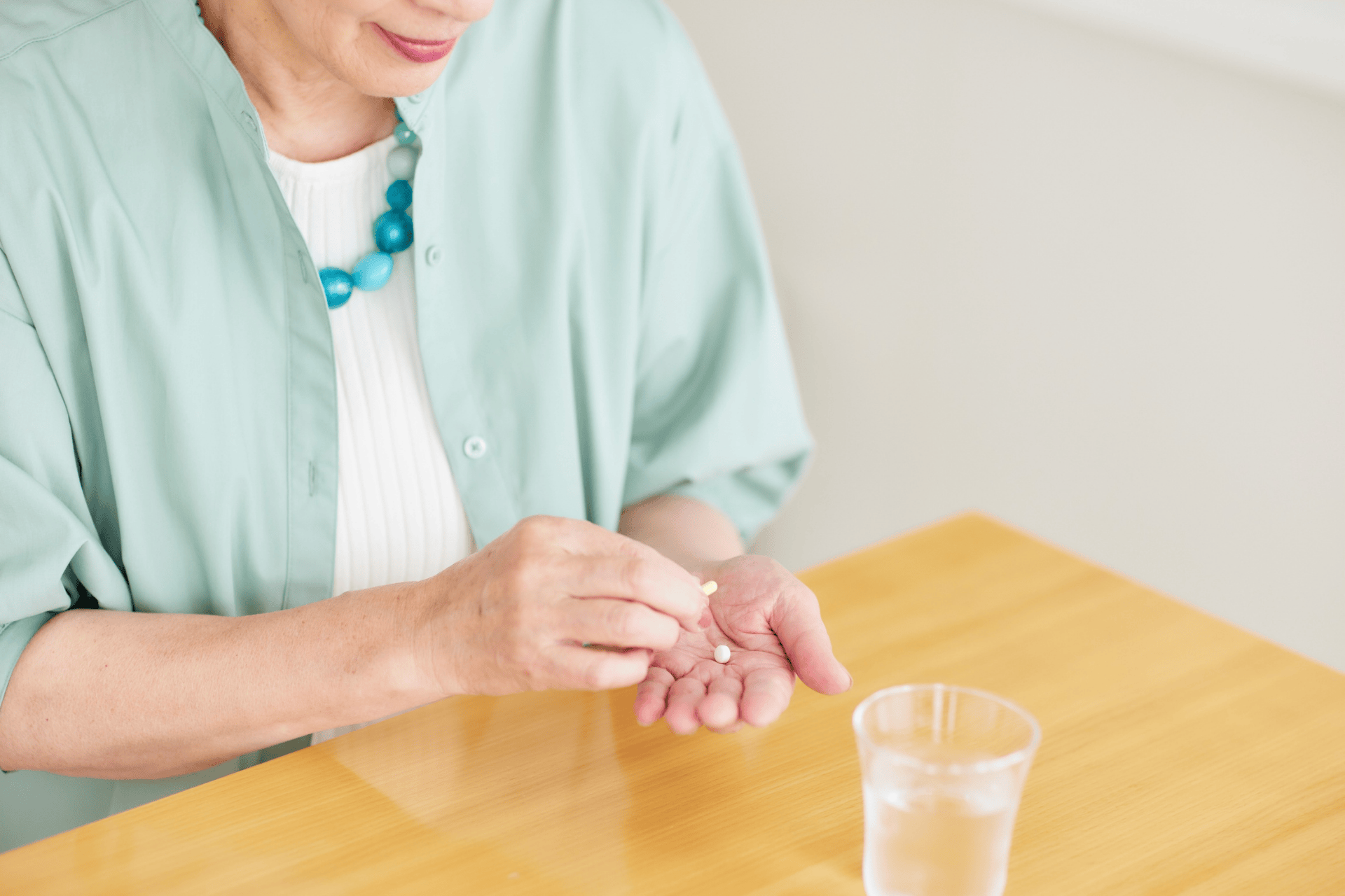 Woman holding pills in her hand with a glass of water on the table.