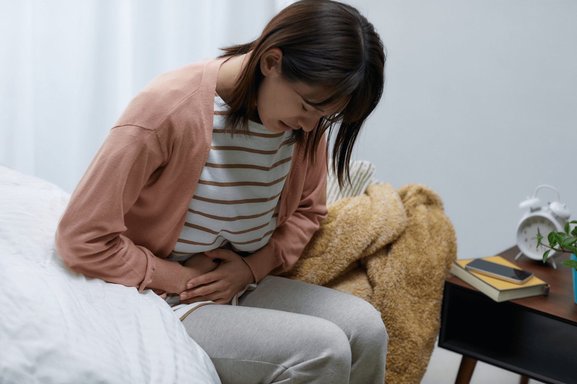 Woman sitting on a bed, clutching her stomach in pain.