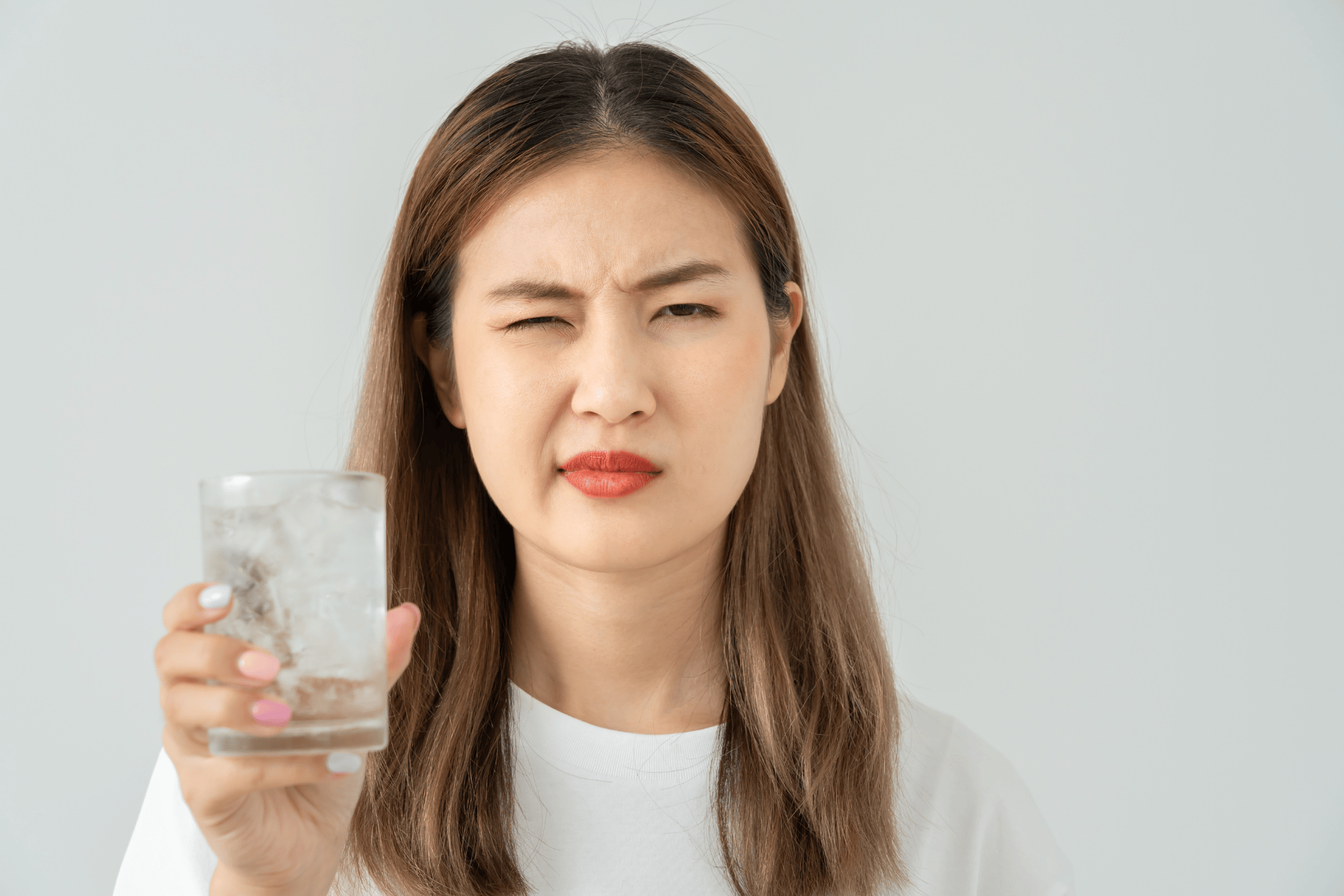 Woman holding a glass of water and wincing with discomfort.