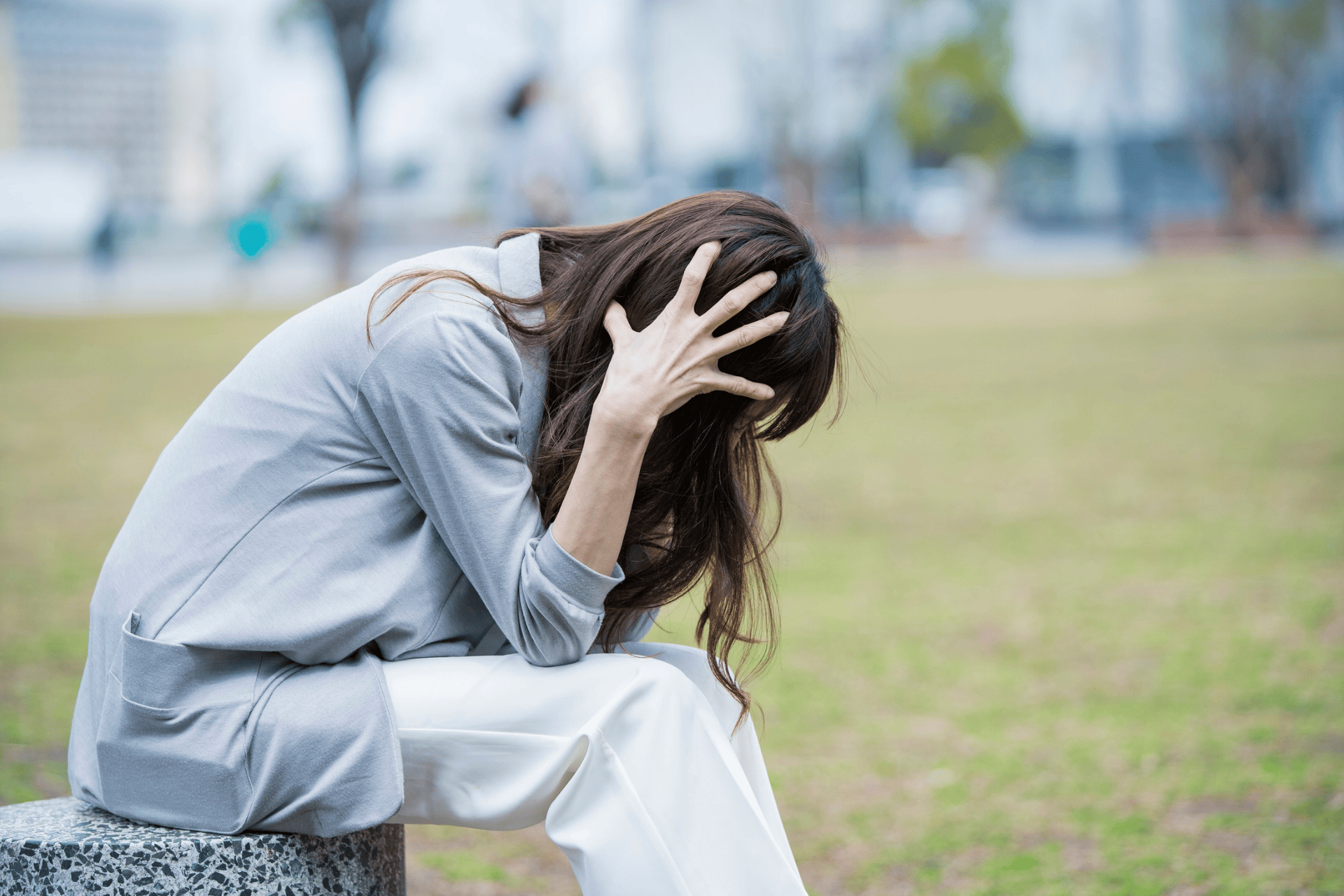Woman sitting outdoors holding her head in distress.