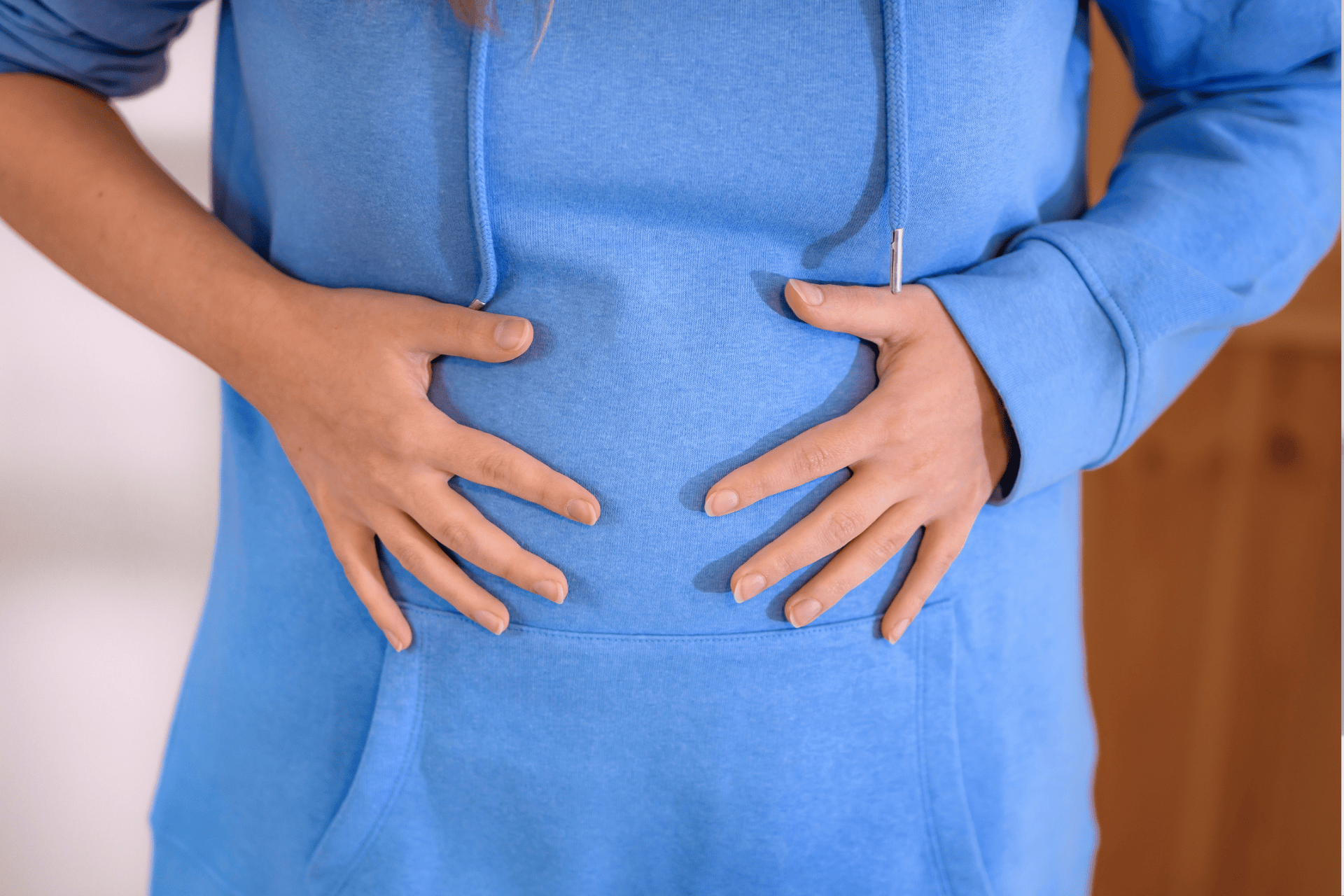 Person in a blue hoodie holding their stomach in discomfort.