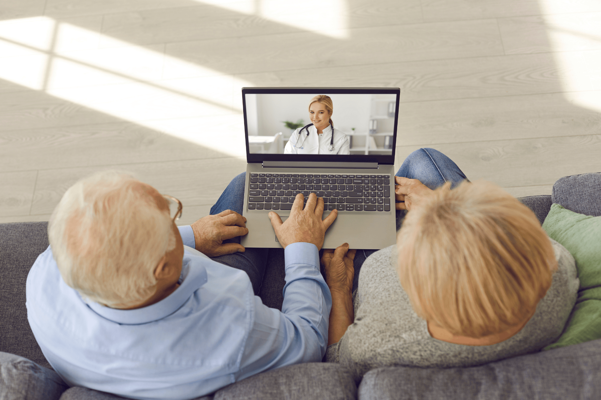 Older couple on couch having an online consultation with a doctor on a laptop.