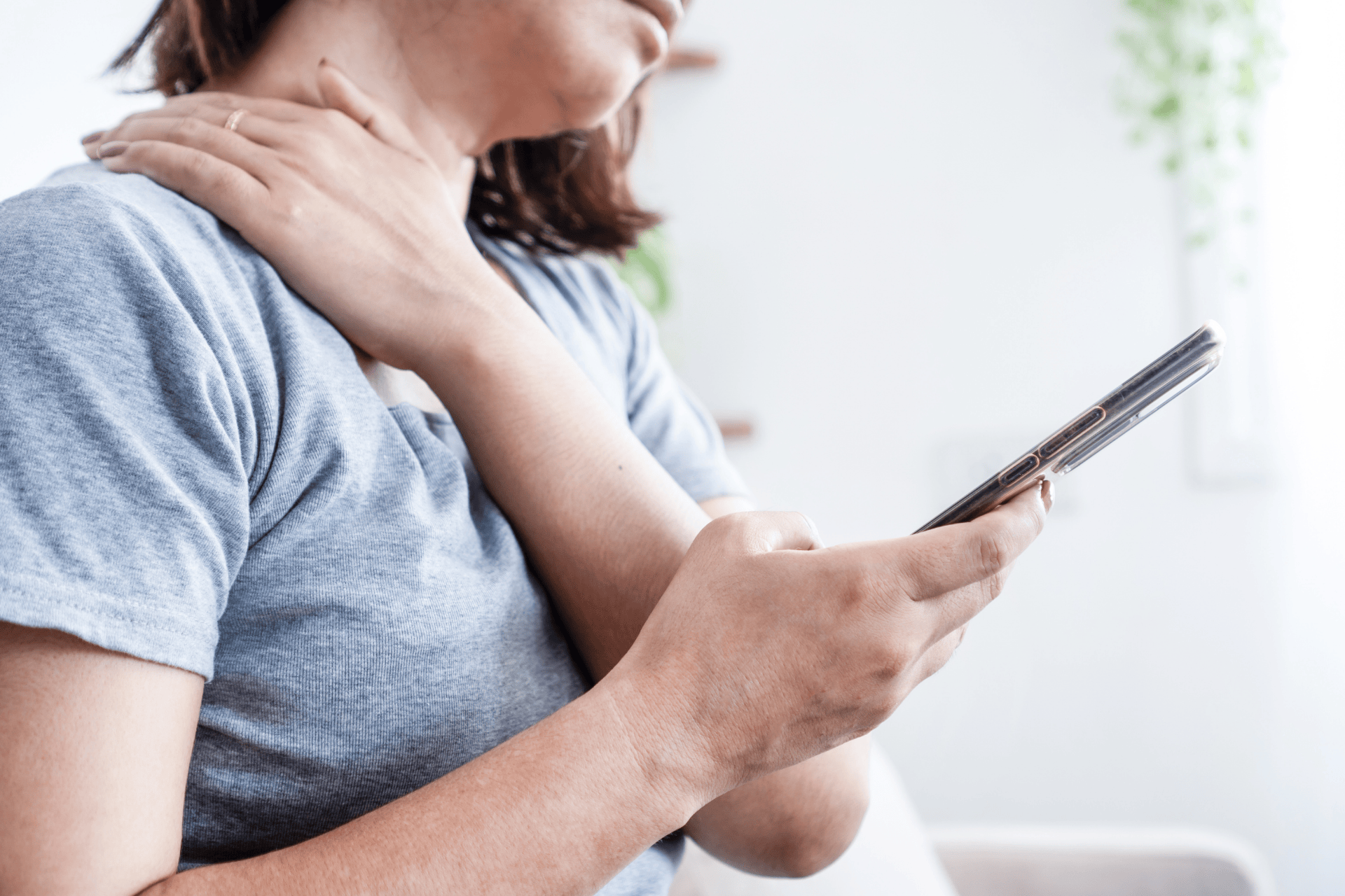 Woman holding her neck in pain while looking at her phone.