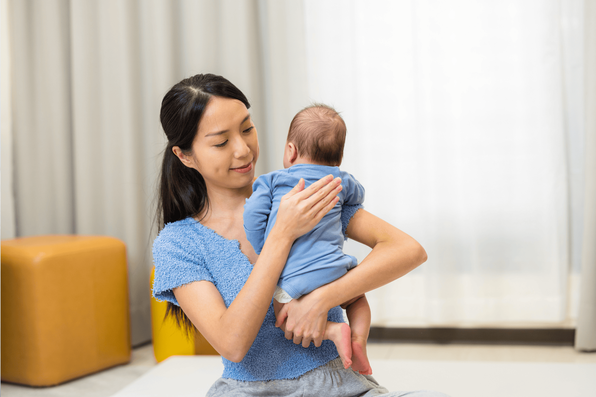 Mother holding and gently patting her baby in a cozy room.