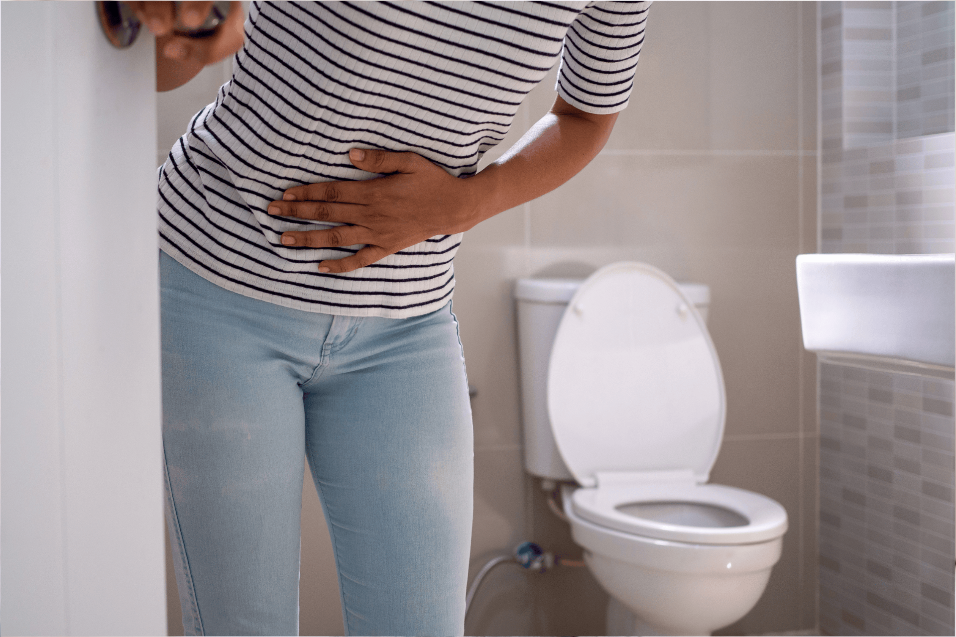 Person clutching stomach in pain while standing near a toilet in a bathroom.