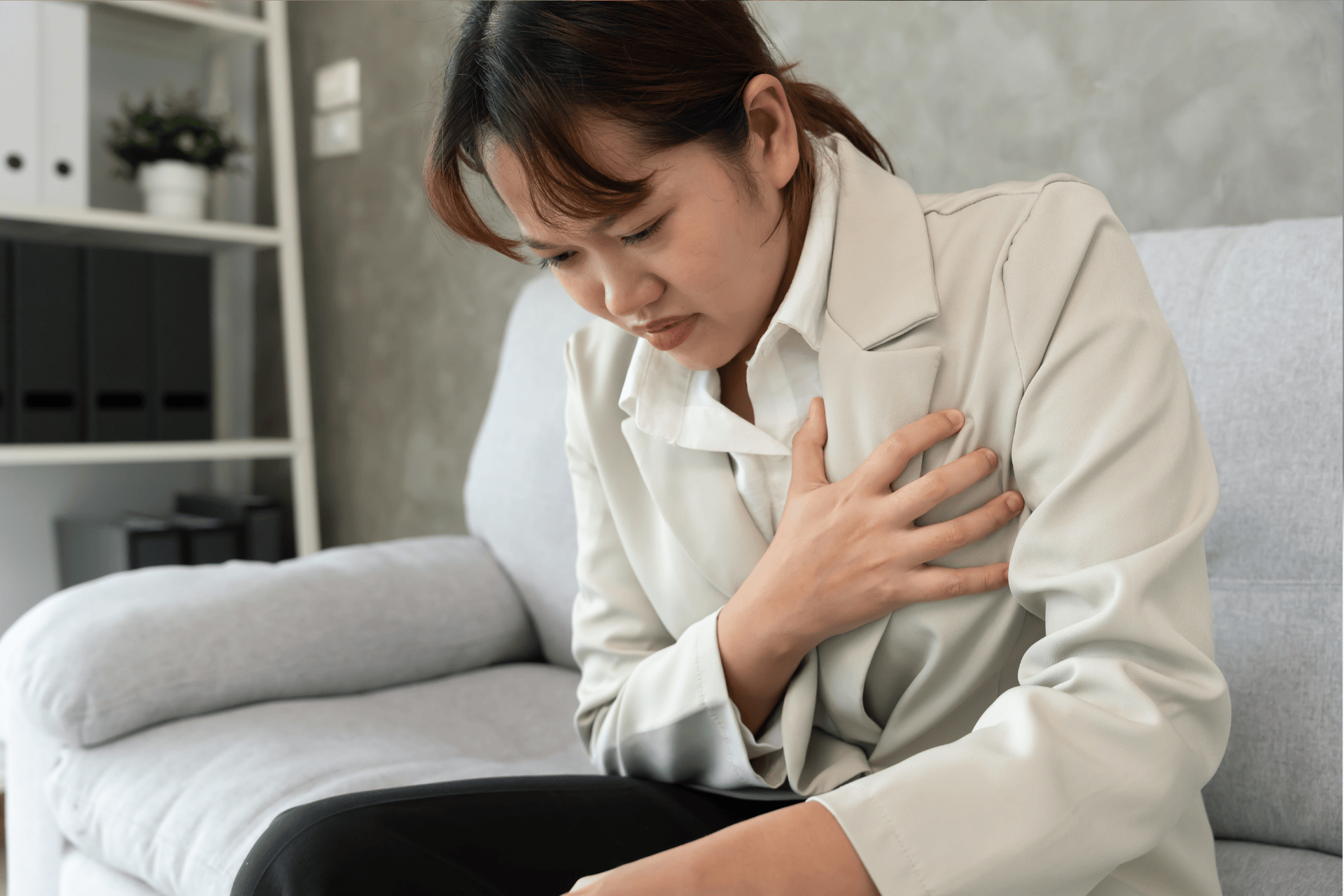 Woman clutching her chest in pain while sitting on a couch.
