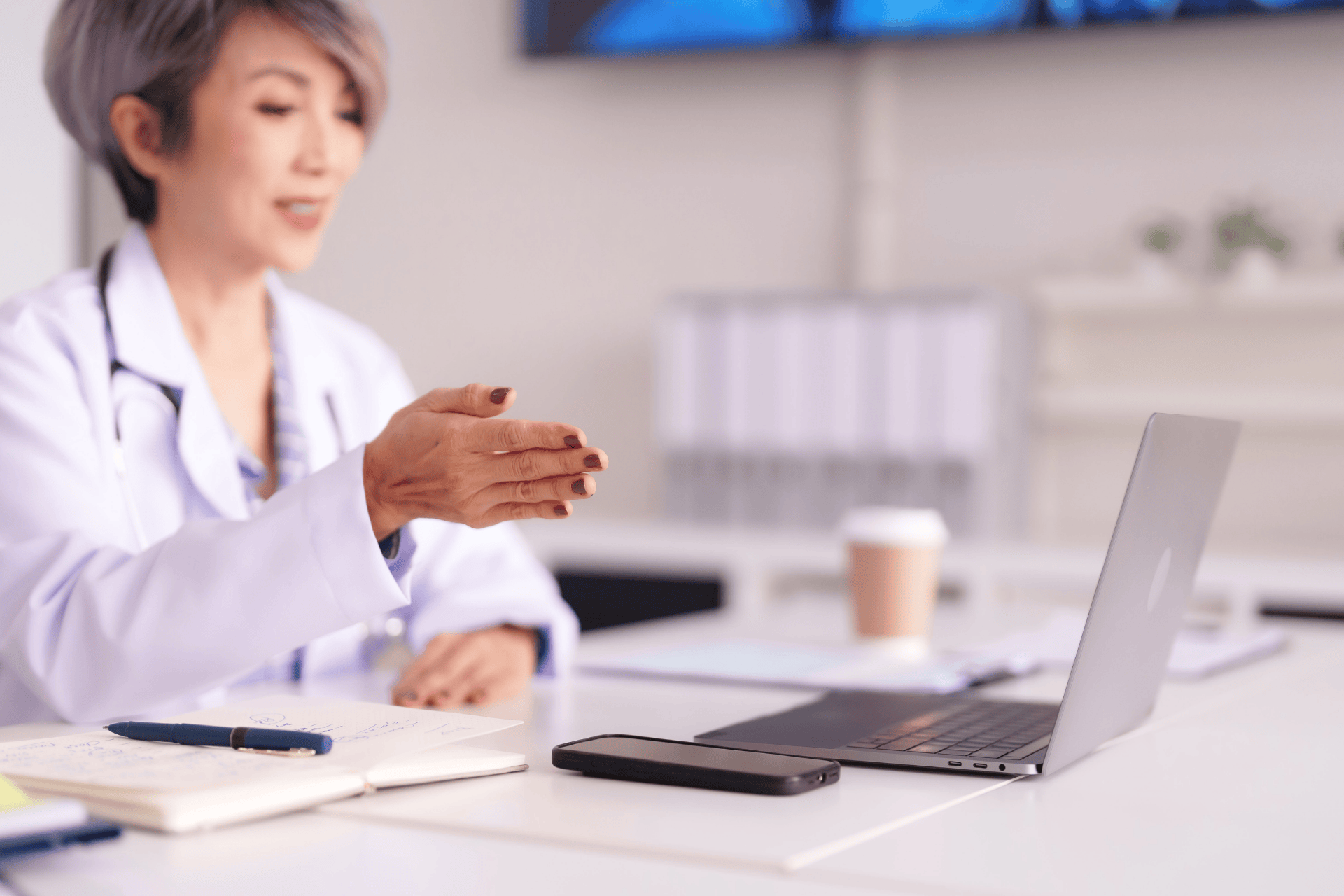 Doctor sitting at a desk, gesturing during an online consultation on a laptop.