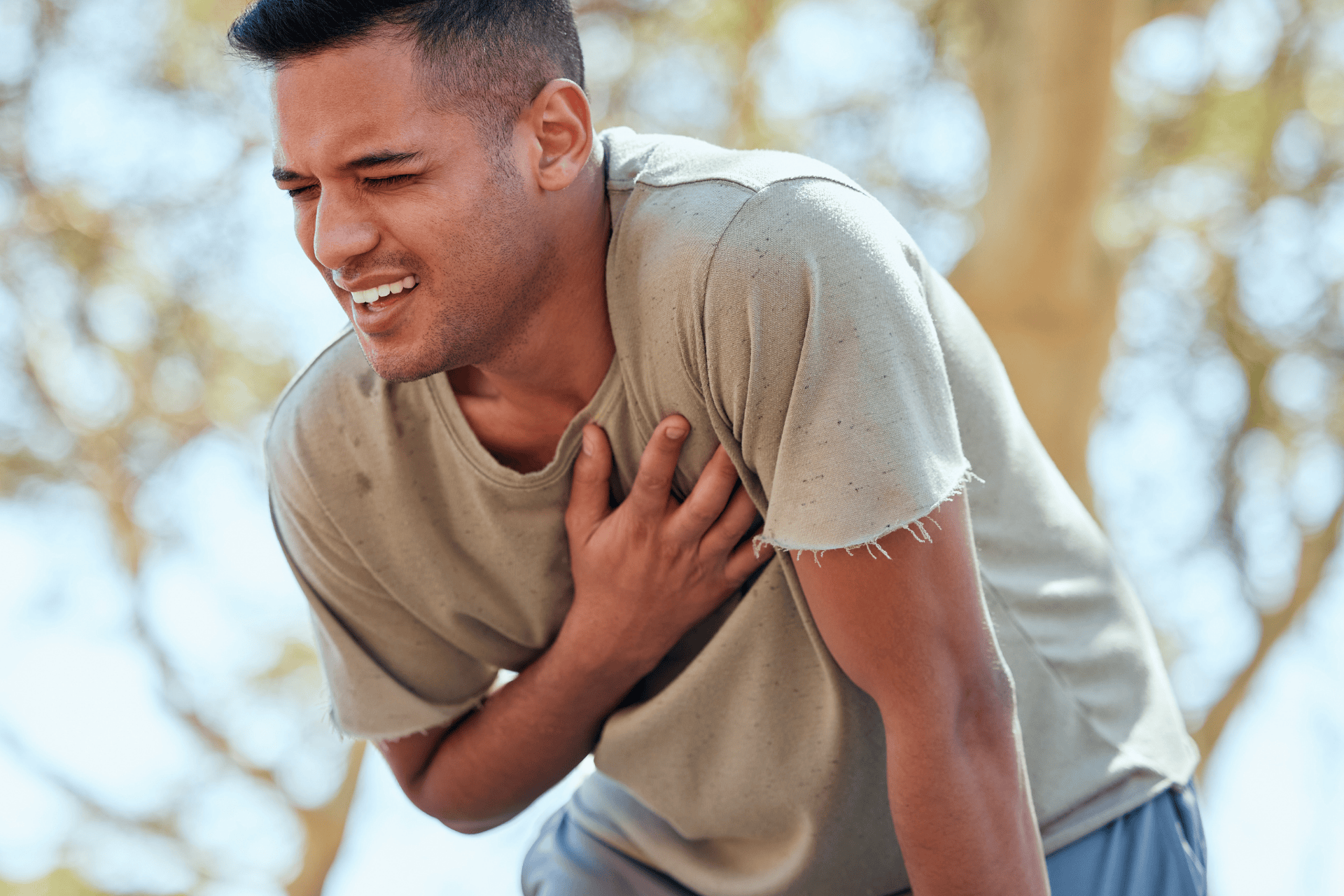 Man clutching his chest in pain while outdoors.