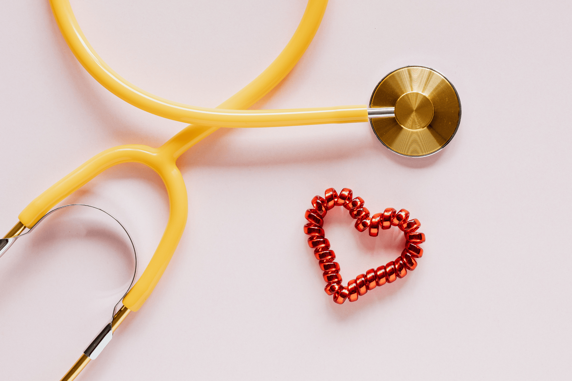 Yellow stethoscope beside a red heart shape on a pink background.