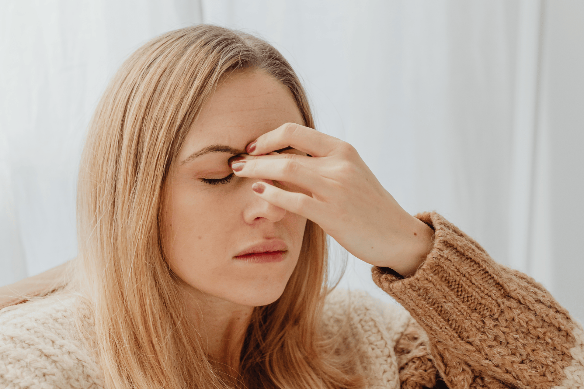 Woman touching her forehead and nose bridge, appearing to have a headache or sinus pain.