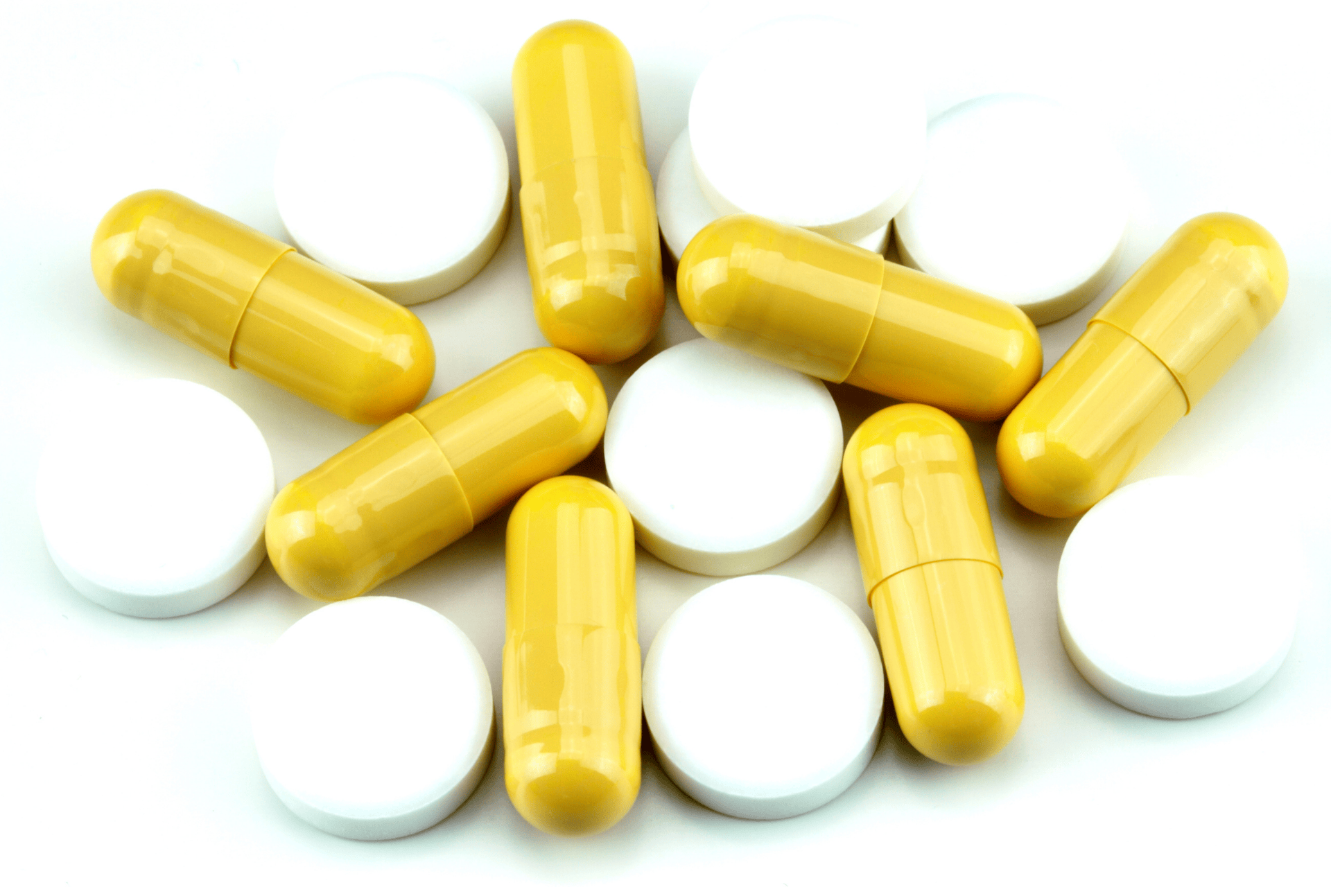 Close-up of yellow capsules and white tablets on a white background.