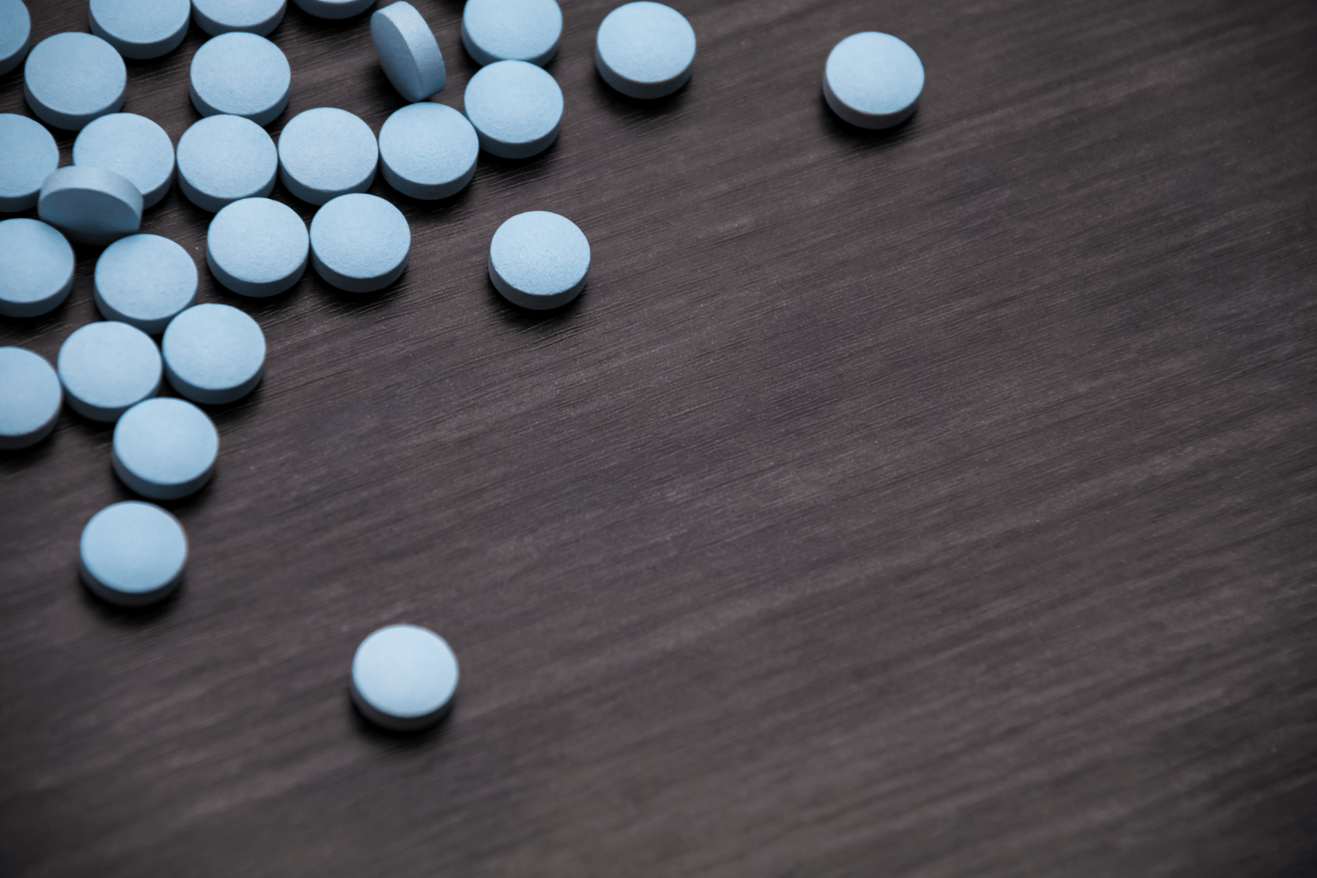 Blue round pills scattered on a dark wooden surface.