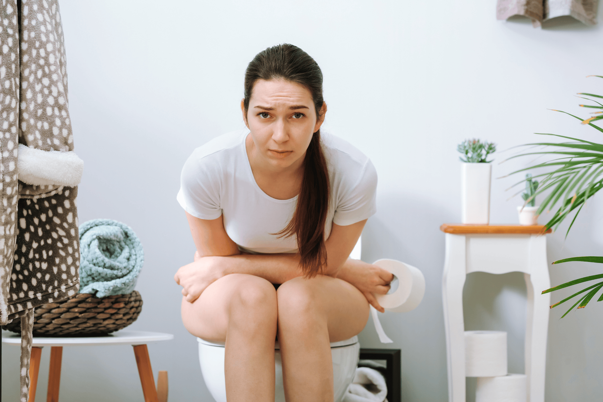 Woman sitting on a toilet looking uncomfortable and holding toilet paper.