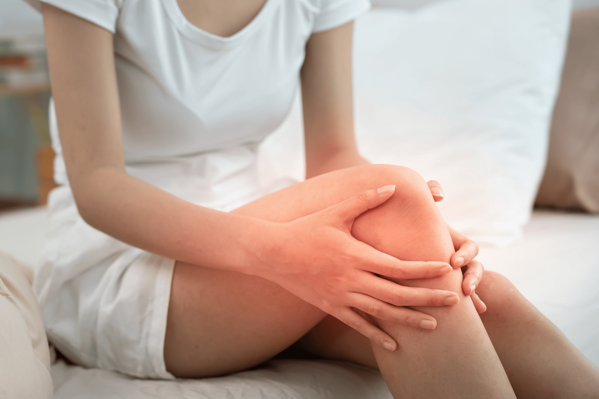 Woman sitting on a bed holding her inflamed knee in discomfort.