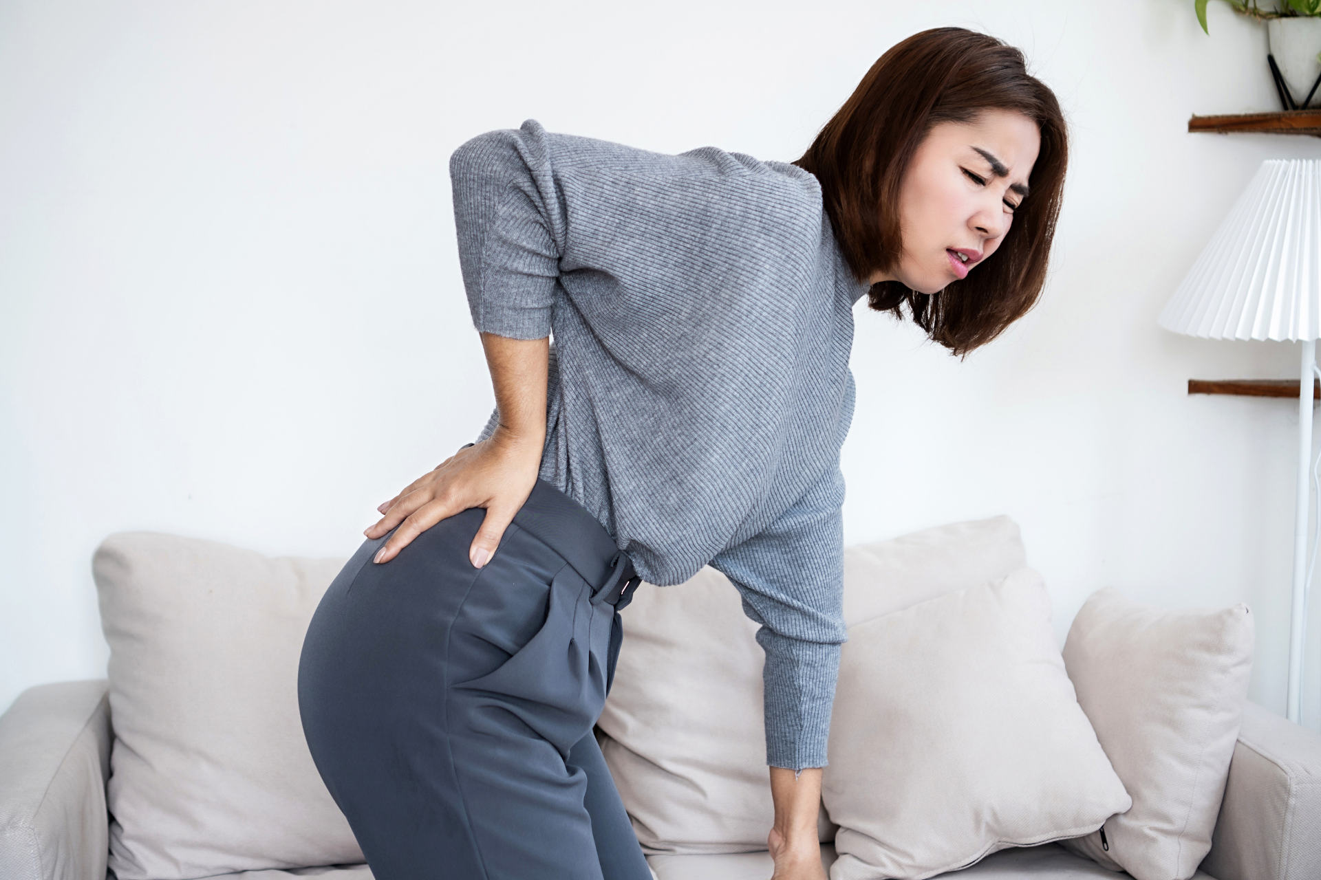 Woman holding her lower back in pain, showing symptoms of sciatica.