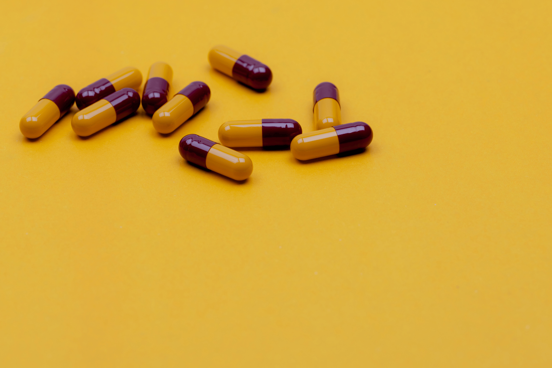 Yellow and maroon capsules scattered on a bright yellow surface.