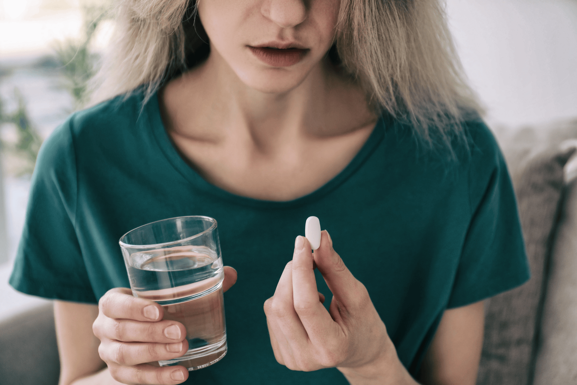 A woman holding a glass of water in one hand and a white pill in the other