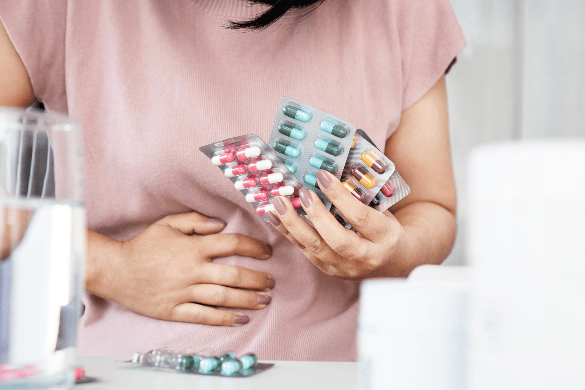 Woman holding her stomach while looking at several packs of pills