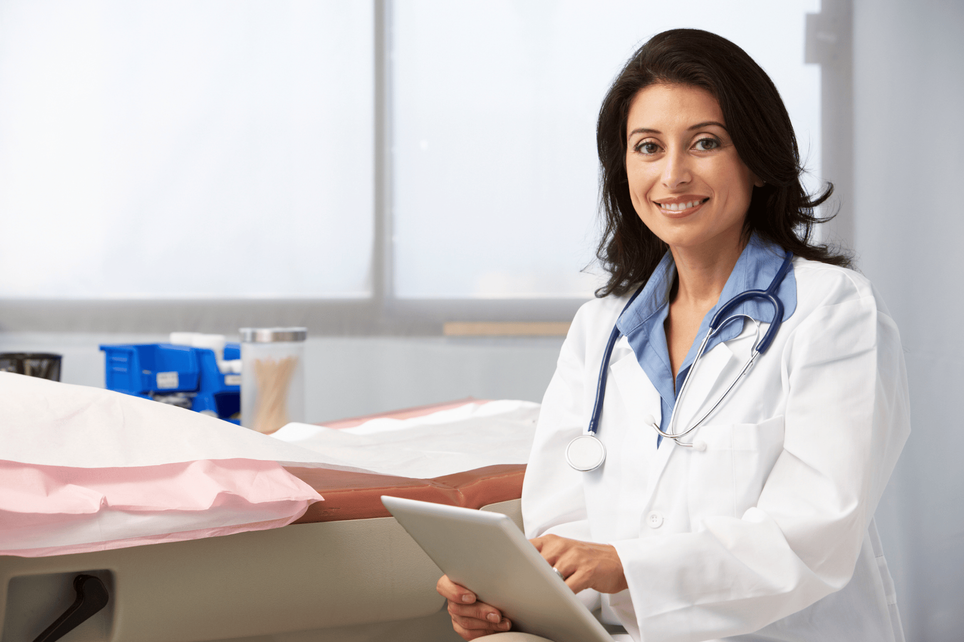 Female doctor smiling while holding a tablet in a medical office.