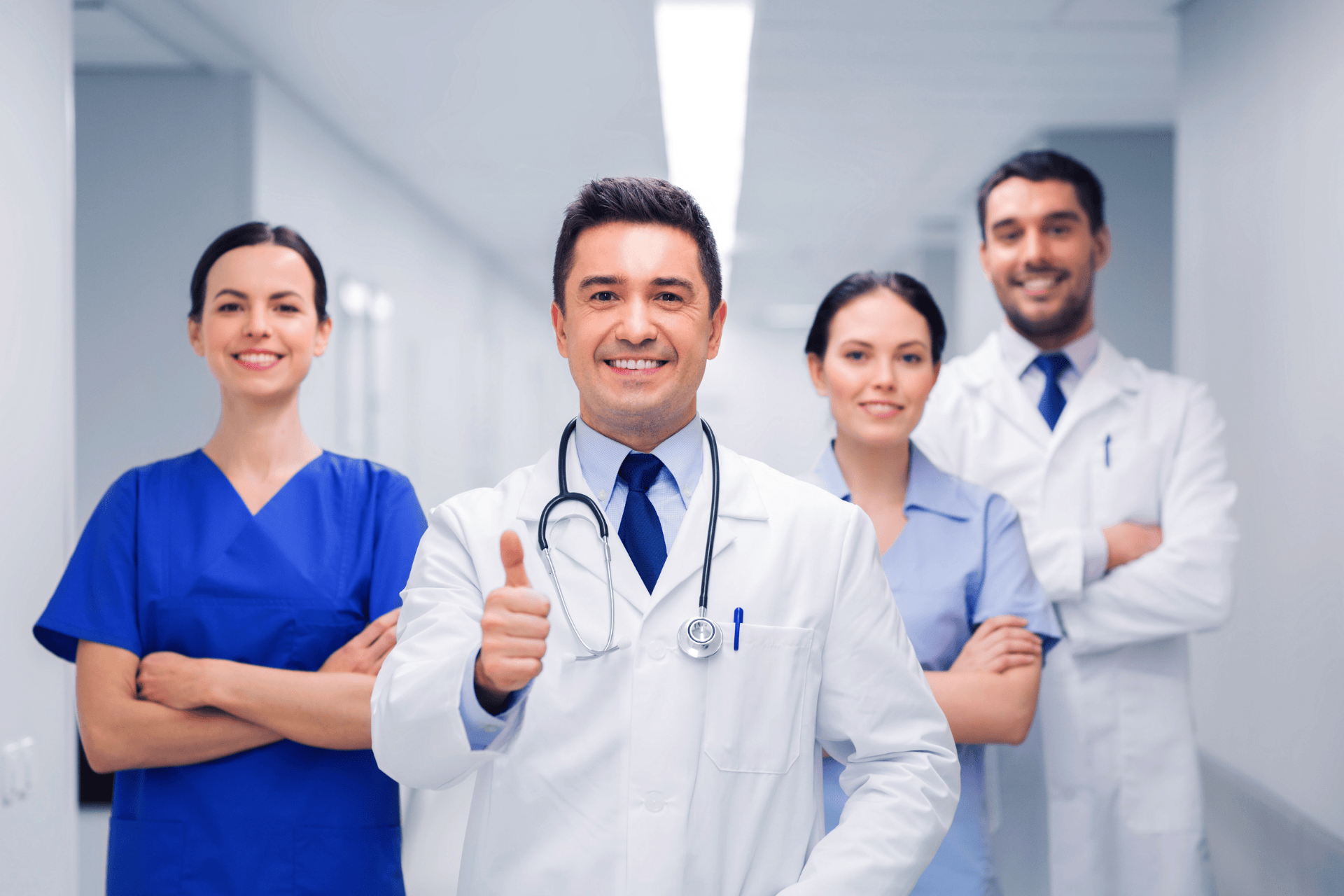 A Group of healthcare professionals standing in a hallway, with a doctor in front giving a thumbs-up.