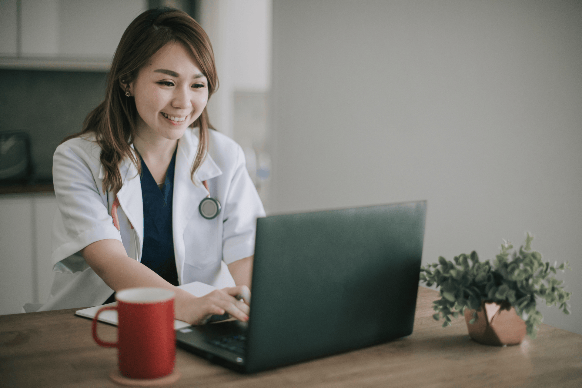Female doctor smiling while working on a laptop at a desk.