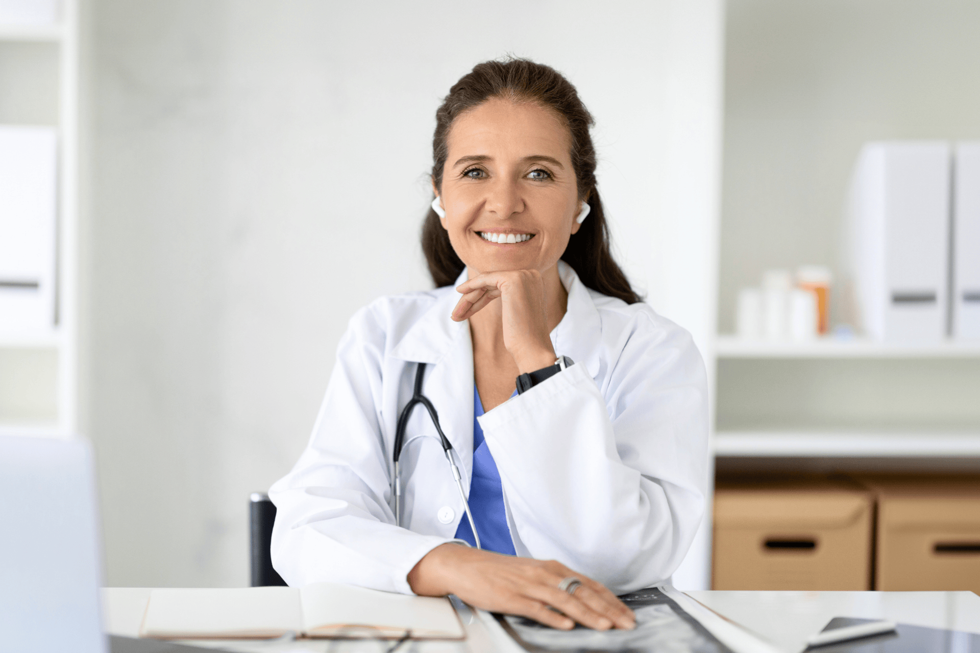 Female doctor smiling while sitting at a desk with a hand resting under her chin.