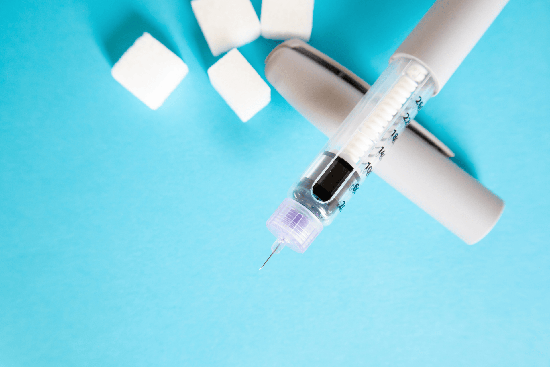 Insulin pen and sugar cubes arranged on a blue background.