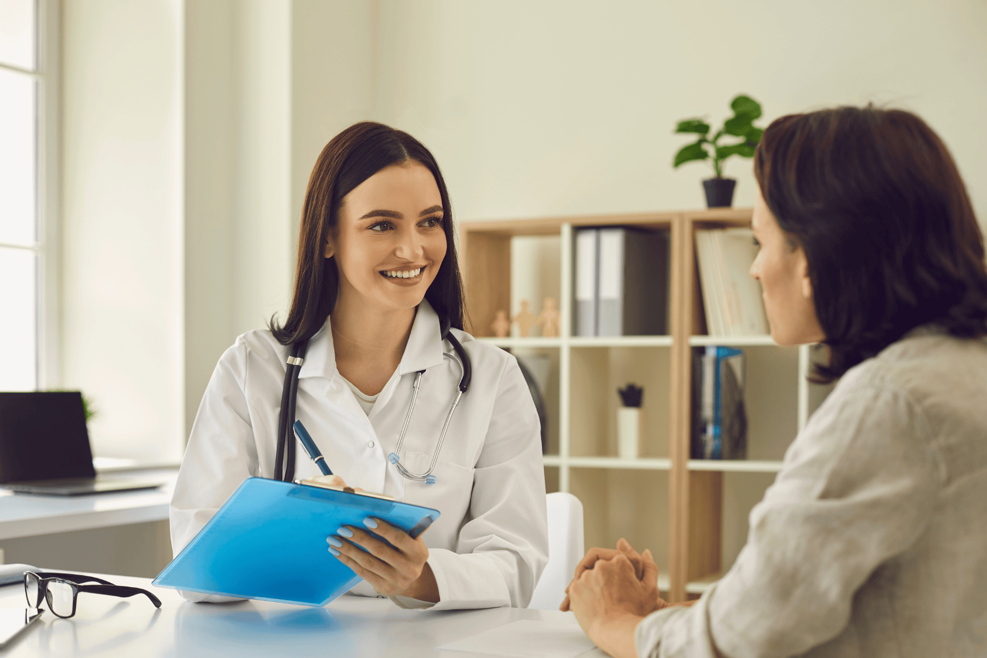 Female doctor smiling while talking with a patient and holding a clipboard.