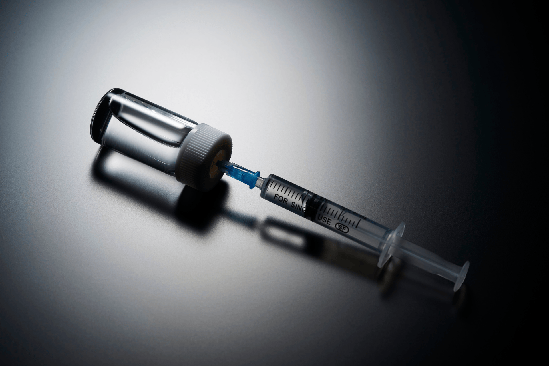 Syringe drawing liquid from a medicine vial on a dark surface.