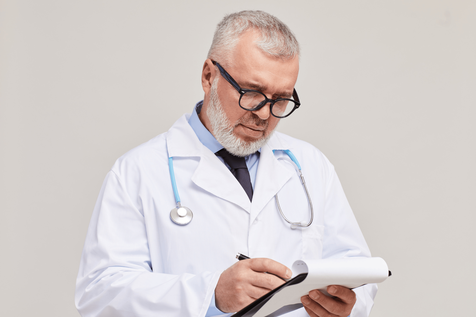 Male doctor with glasses writing on a clipboard.