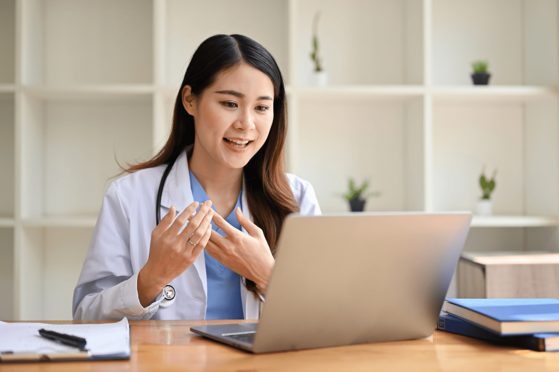 Female doctor talking during an online video call while sitting at her desk with a laptop.