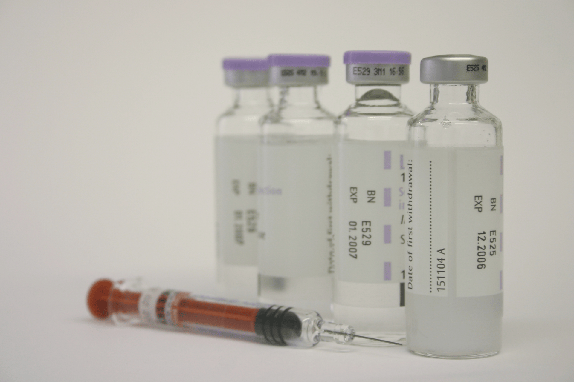 Row of medication vials with a filled syringe lying in front.