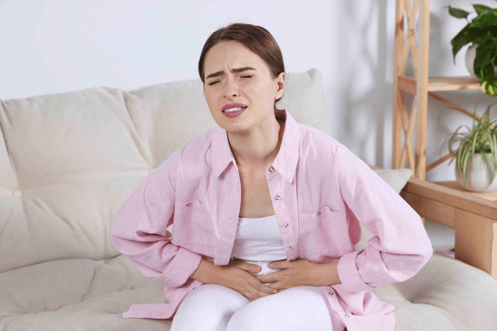 Young woman sitting on a couch holding her stomach in pain.