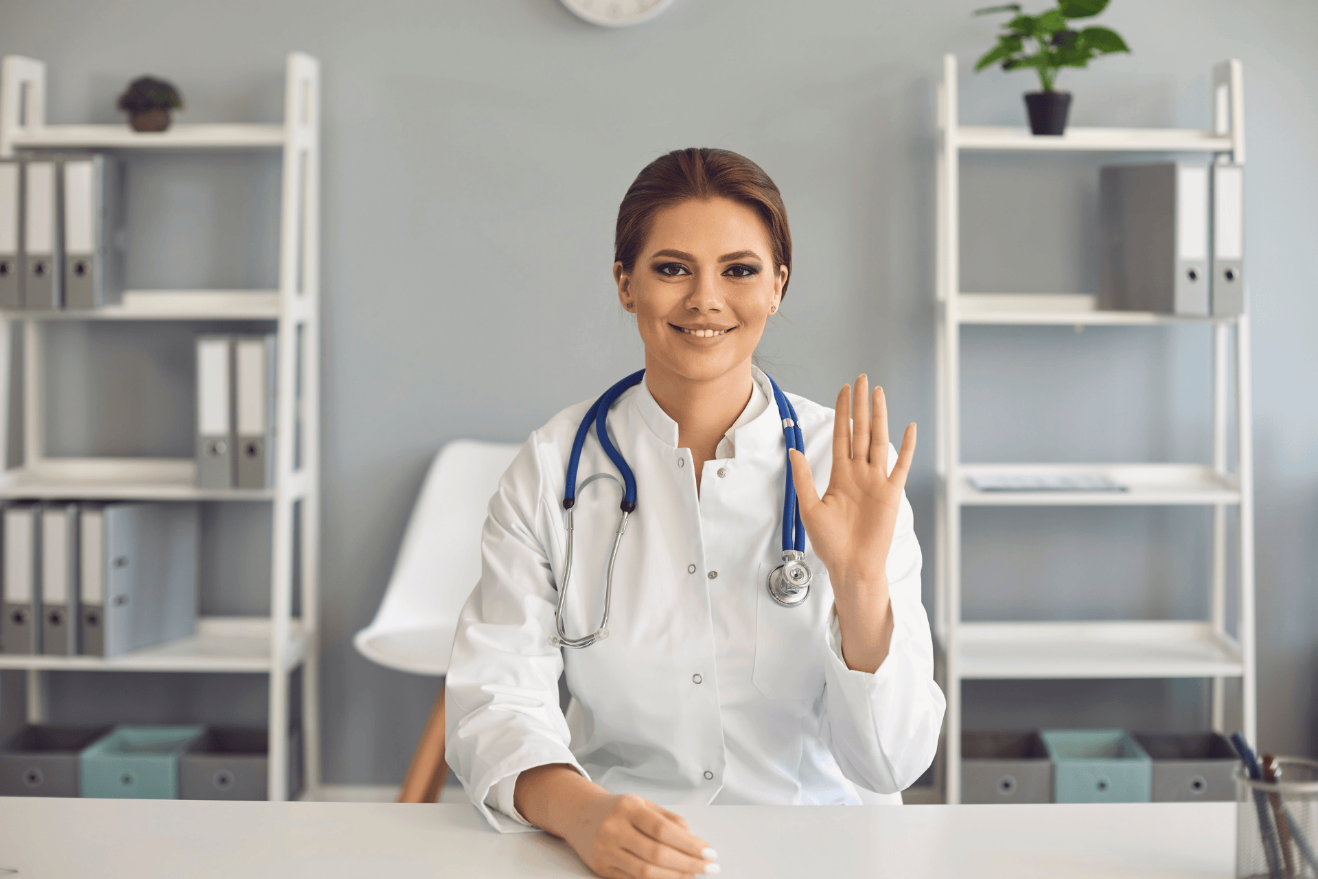 Female doctor in a white coat waving with a friendly smile.
