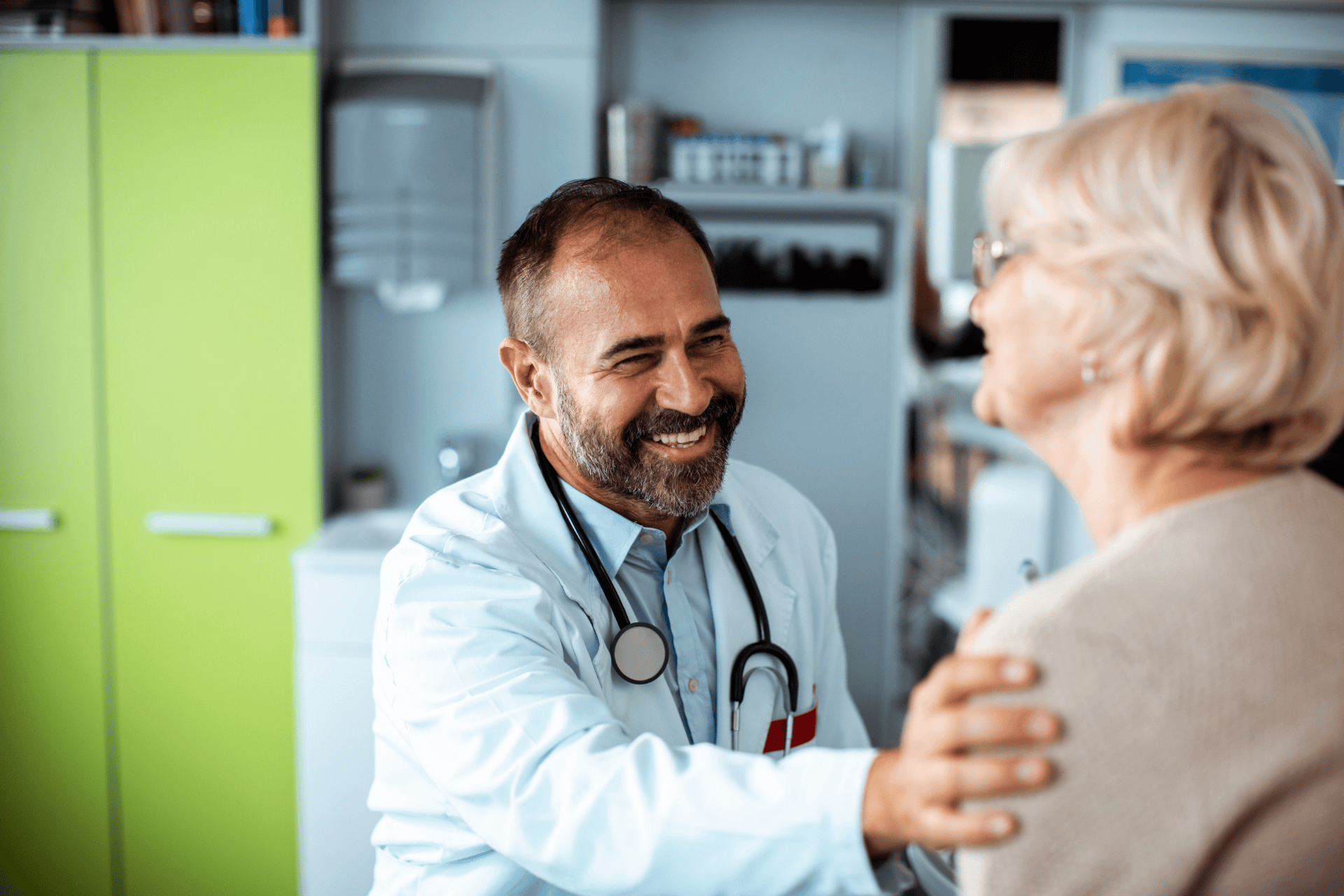 Smiling doctor gently holding an older woman's shoulder during a consultation.
