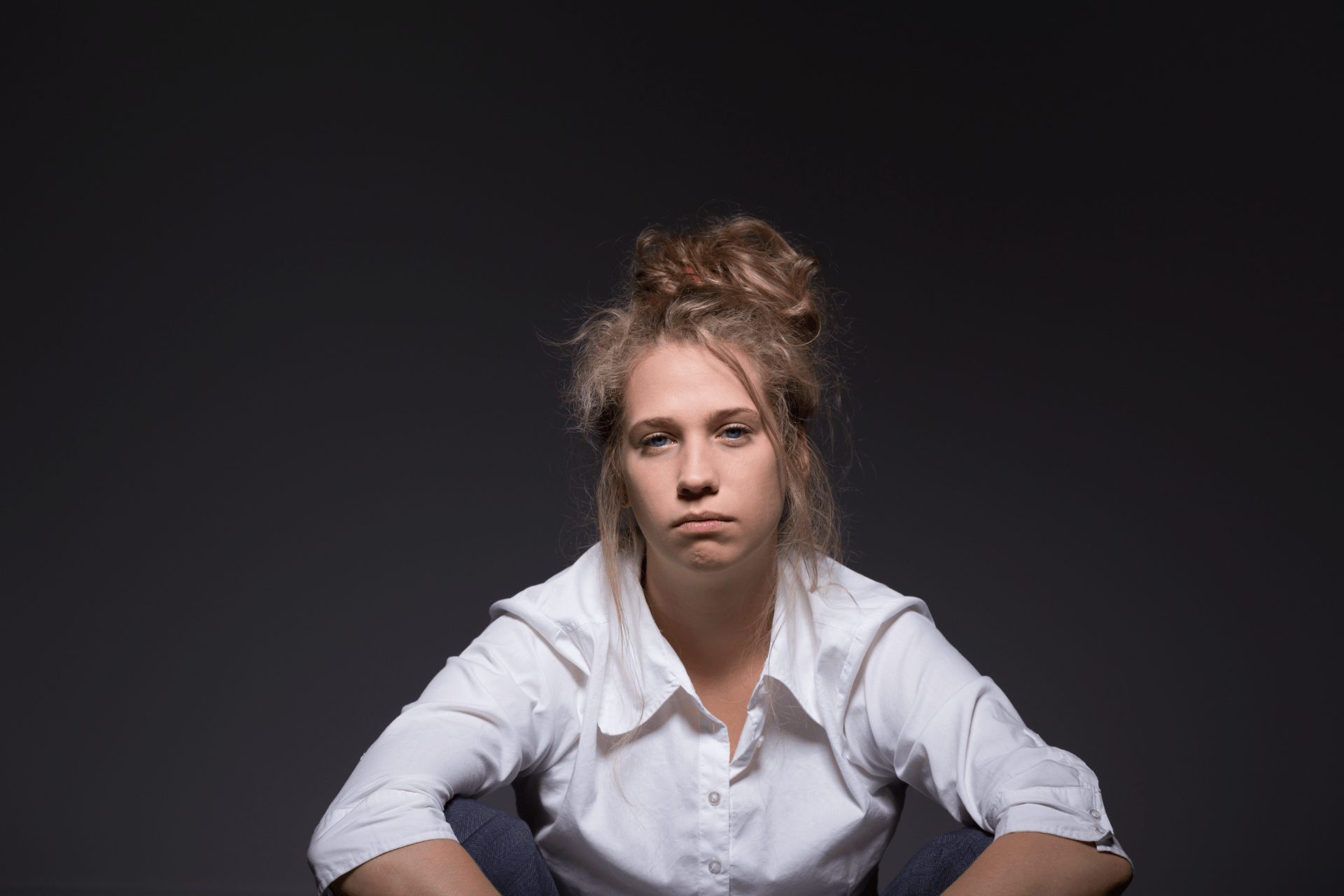 Woman looking exhausted and fatigued while sitting with a tired expression in a dark setting.