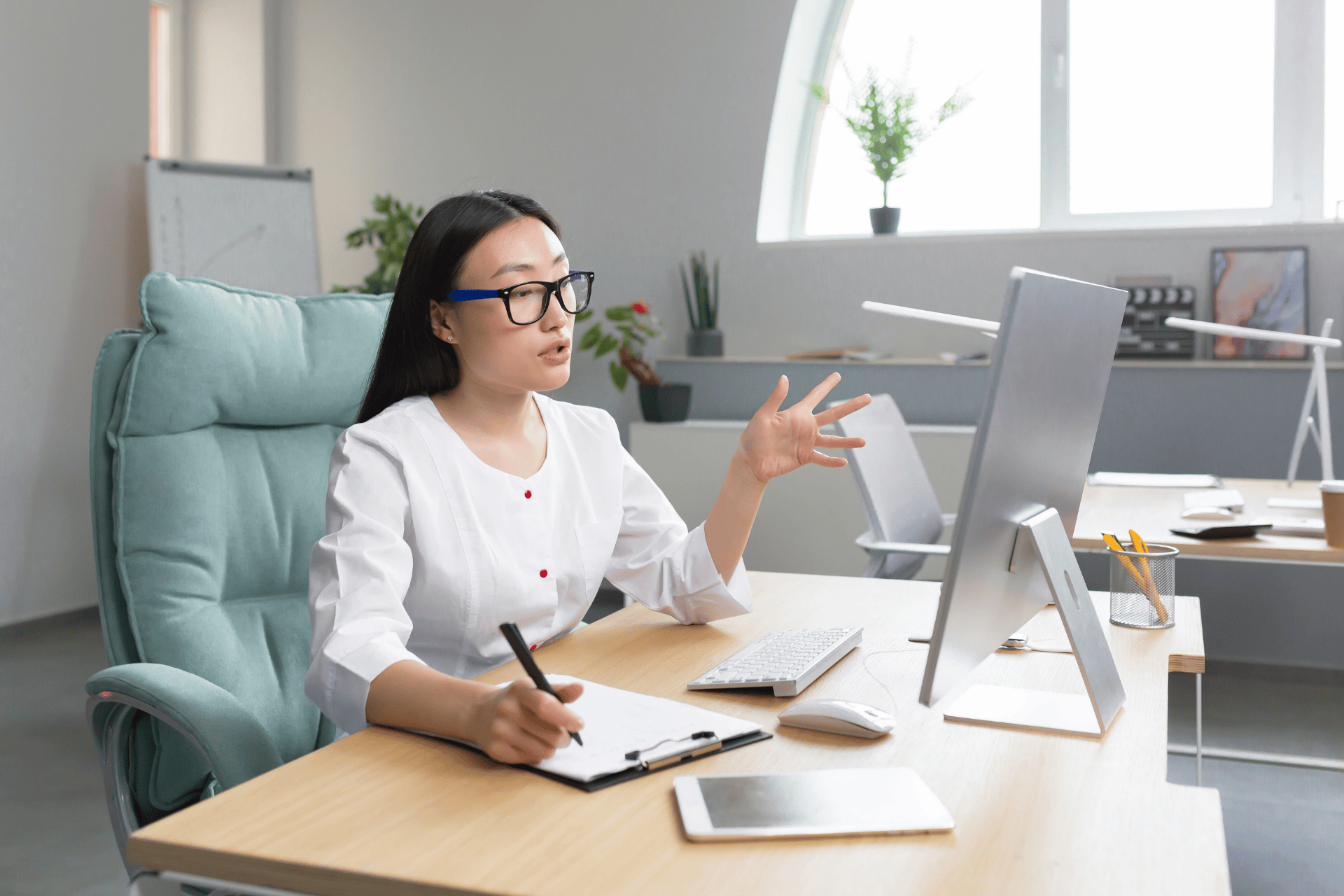 Female doctor on a video call taking notes at her desk.