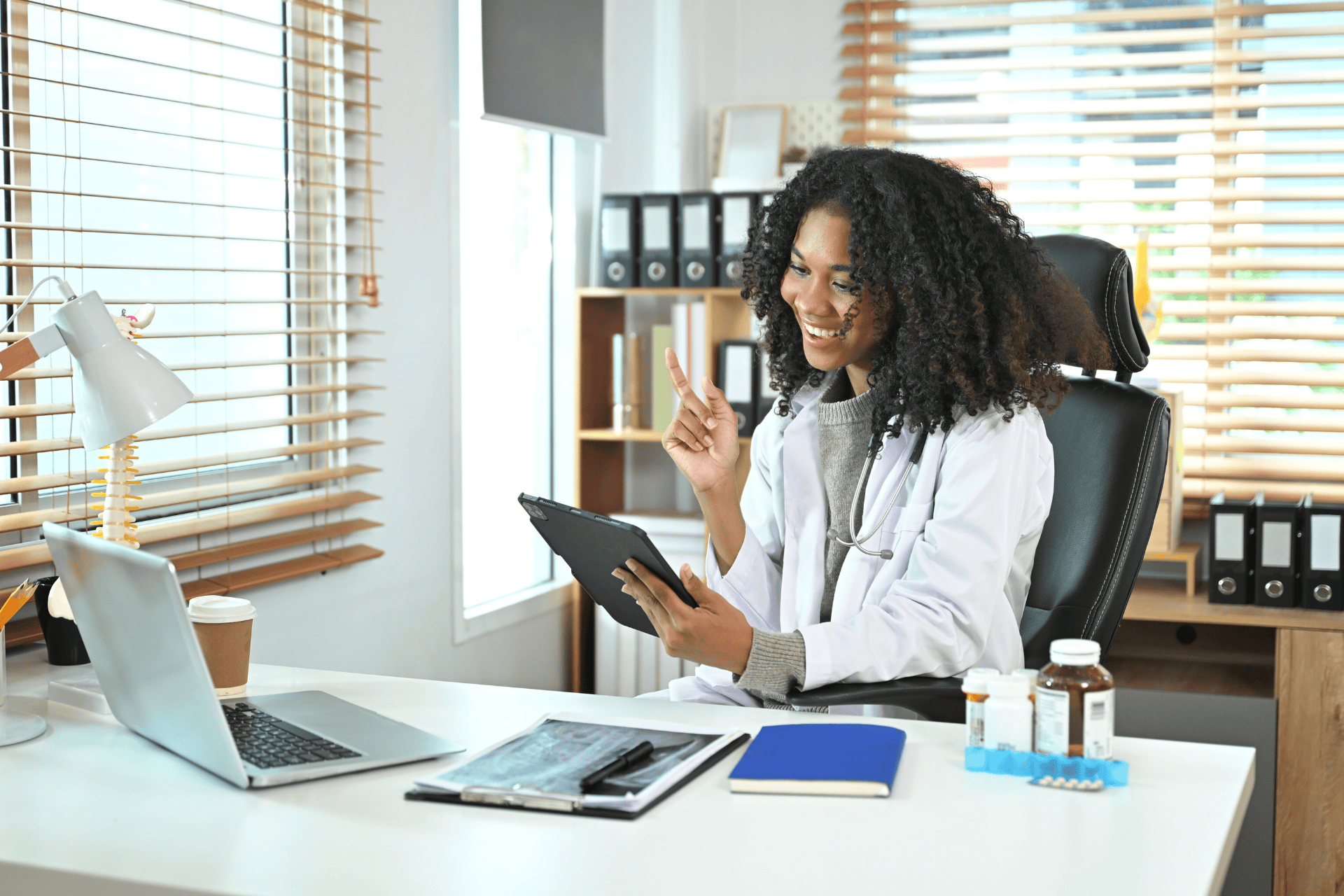 Female doctor smiling while video chatting on a tablet at her desk.