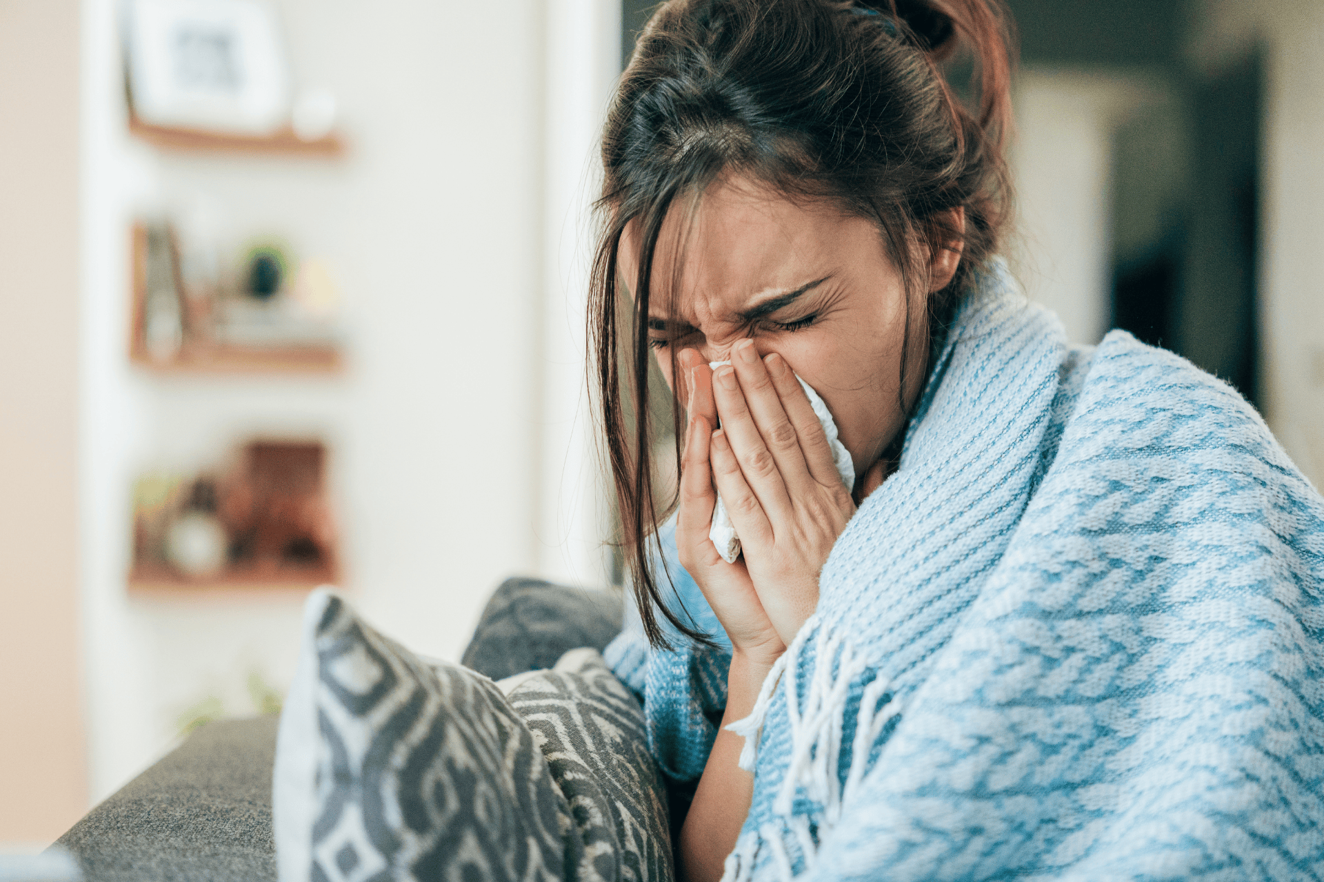 Sick woman wrapped in a blanket, sneezing into a tissue.