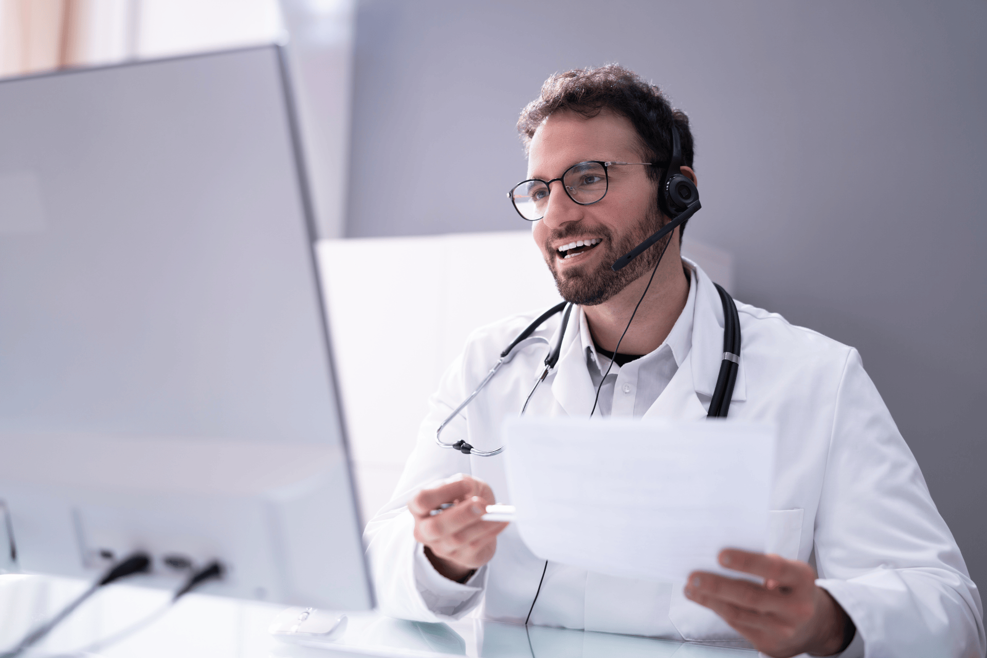Male doctor with a headset smiling while speaking during a telehealth video call.