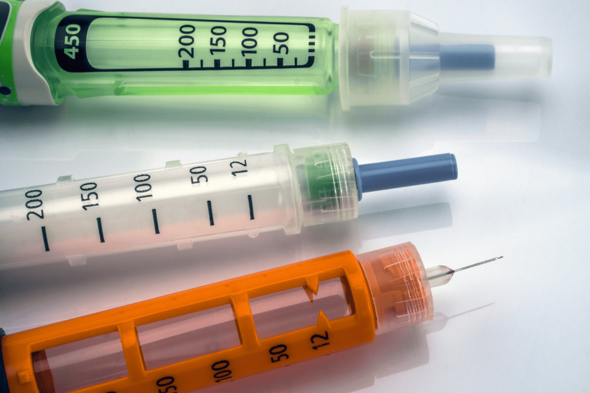 Close-up of three colorful medical injection pens with dosage markings.