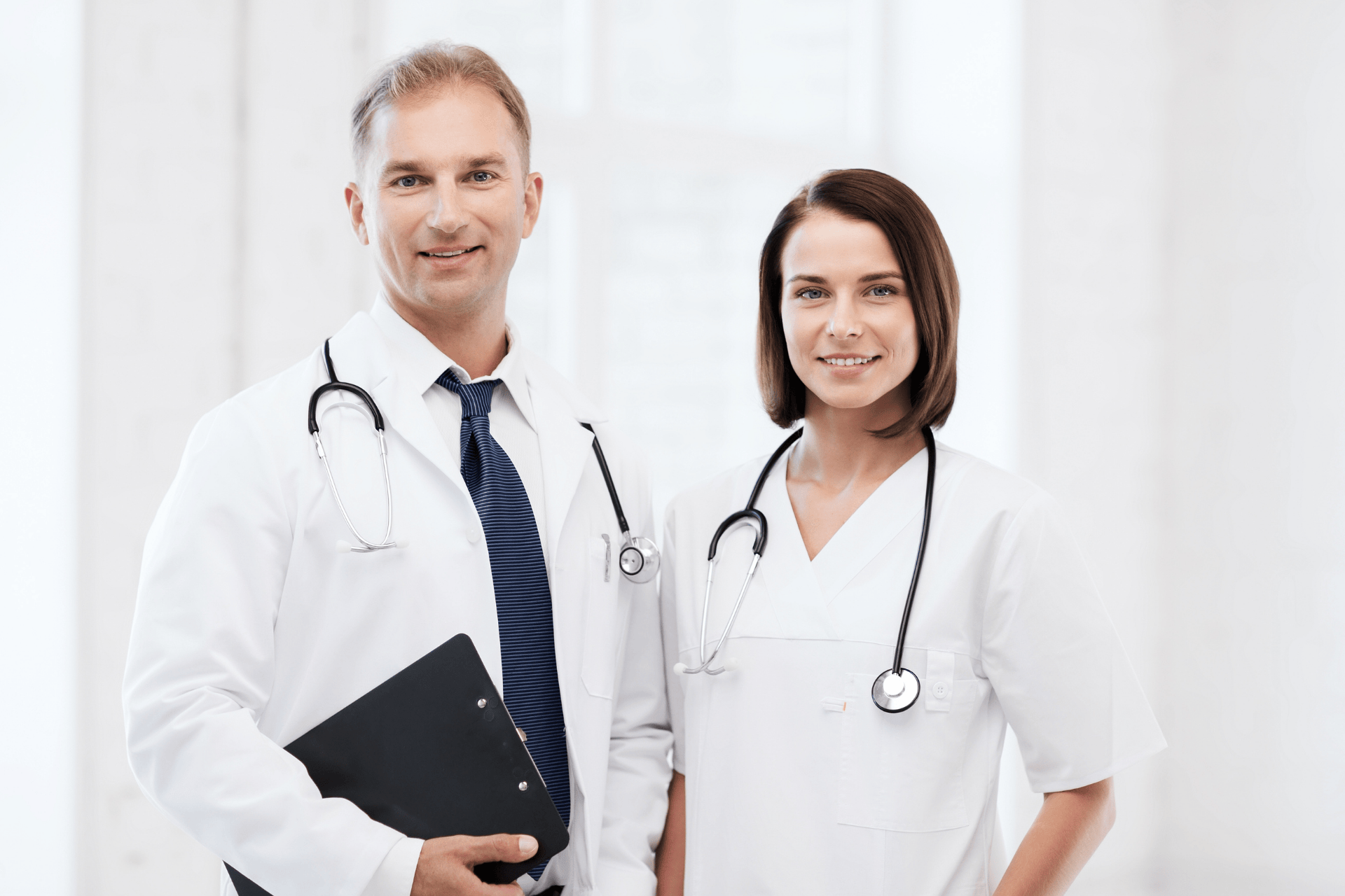 Two doctors wearing white coats and stethoscopes standing side by side and smiling.