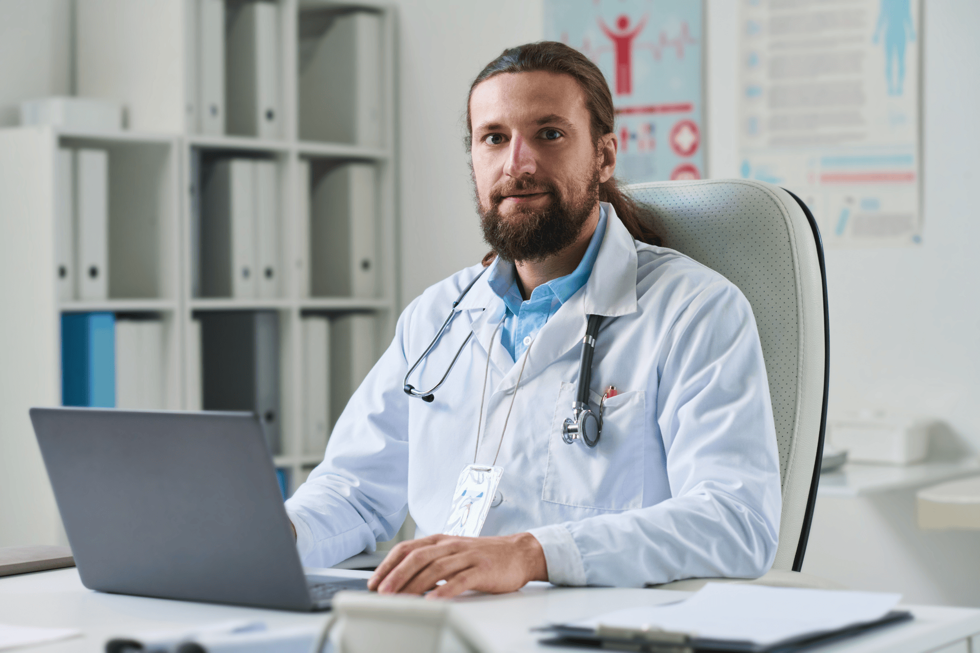Male doctor sitting at a desk working on a laptop.