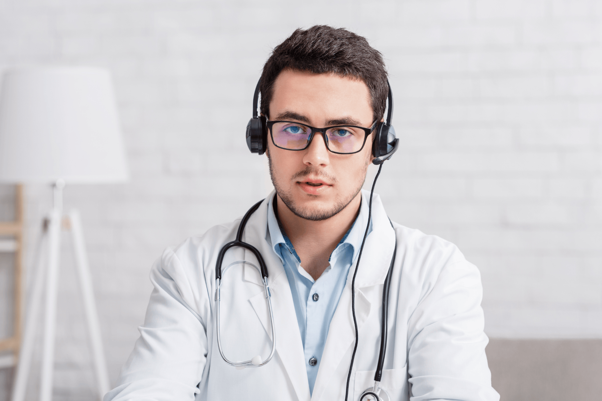 Male doctor wearing a headset and stethoscope, looking at the camera during a virtual consultation.