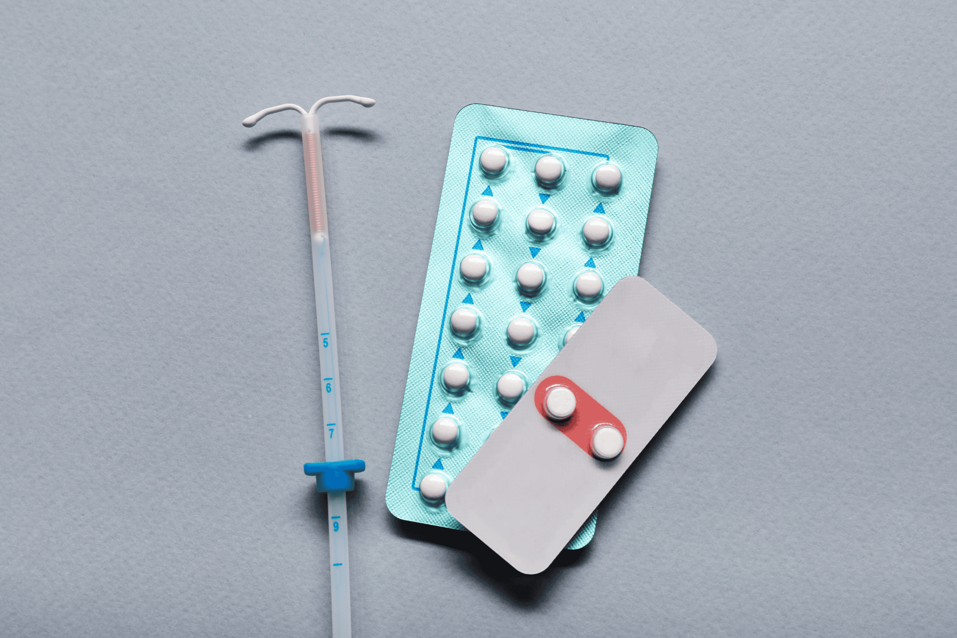 Birth control options, including an IUD and packs of contraceptive pills, on a gray background.