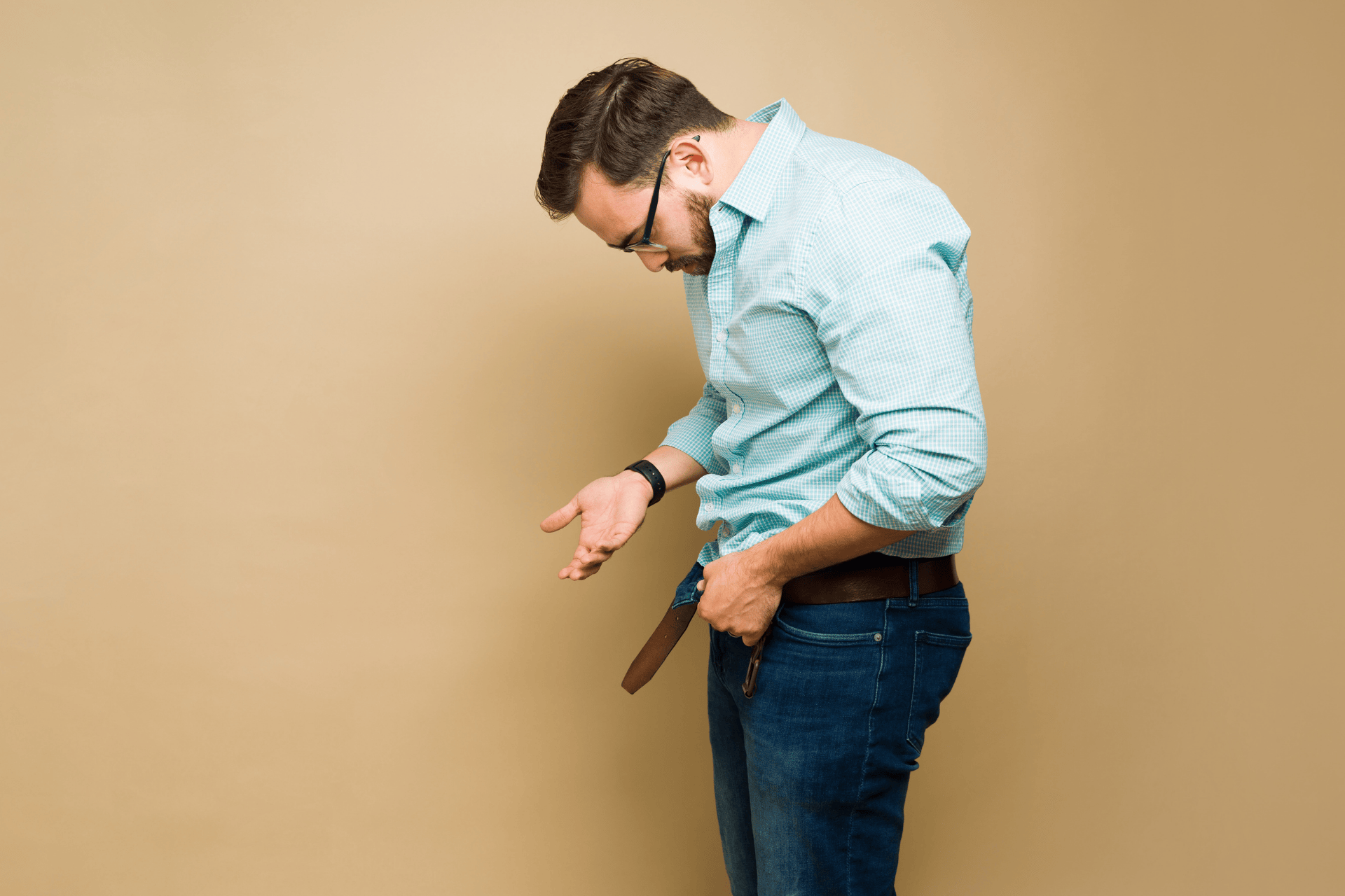 Man looking down at his unbuckled pants, appearing concerned about erectile dysfunction.